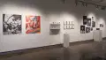 Two large vinyl photographic collages, one in black and white and one in color, are attached to a wall in gallery one. Beside them, two wall shelves hold rows of ceramic mugs with images printed on them. The shelves are mounted beside two rows of square framed photographs. To their right, a monitor is hung, with vinyl prints arranged in a collage-like manner.