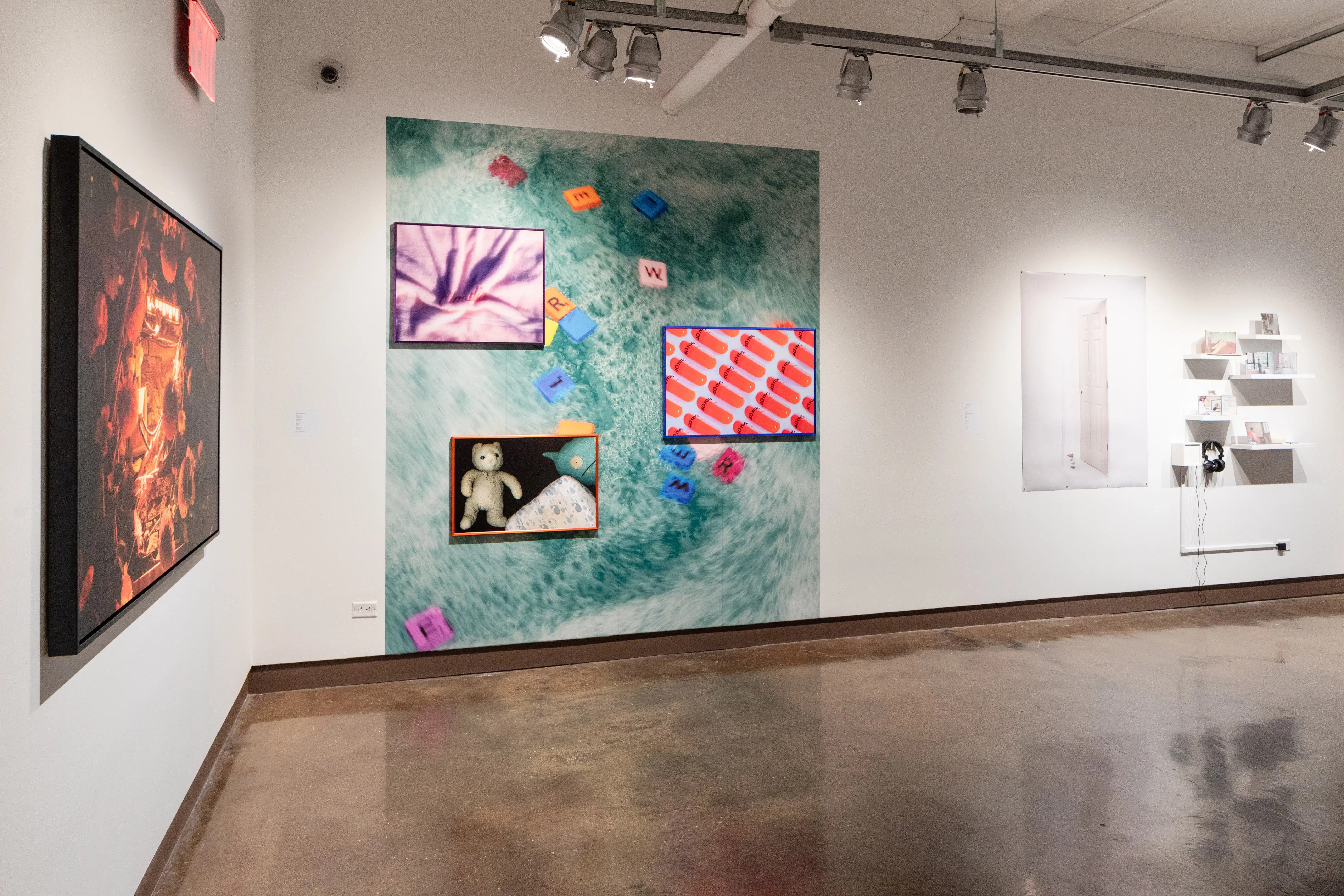 installation shot of framed work, objects on shelves, and a vinyl wall image