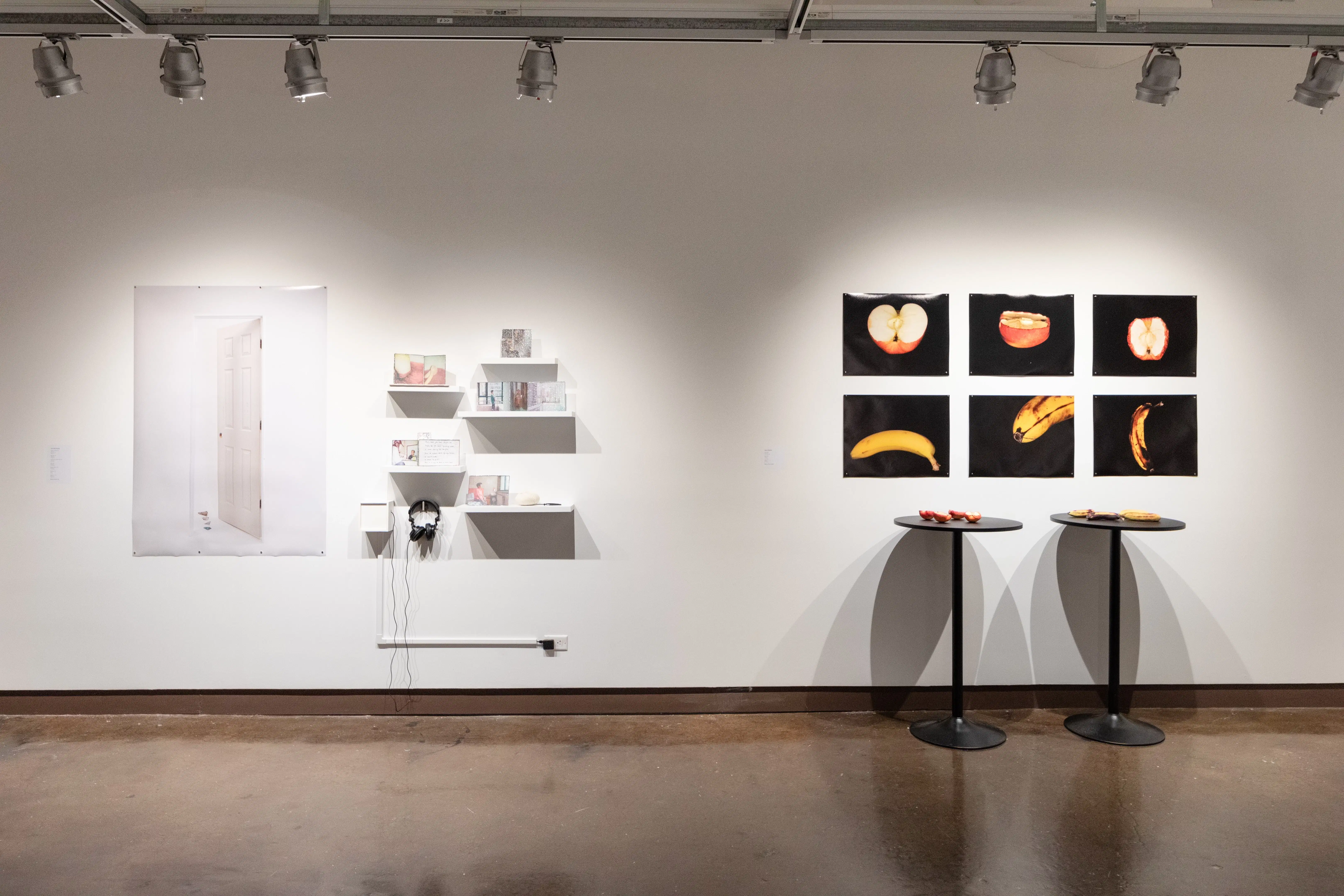 installation shot of unframed prints, tables with 3D objects, and shelves