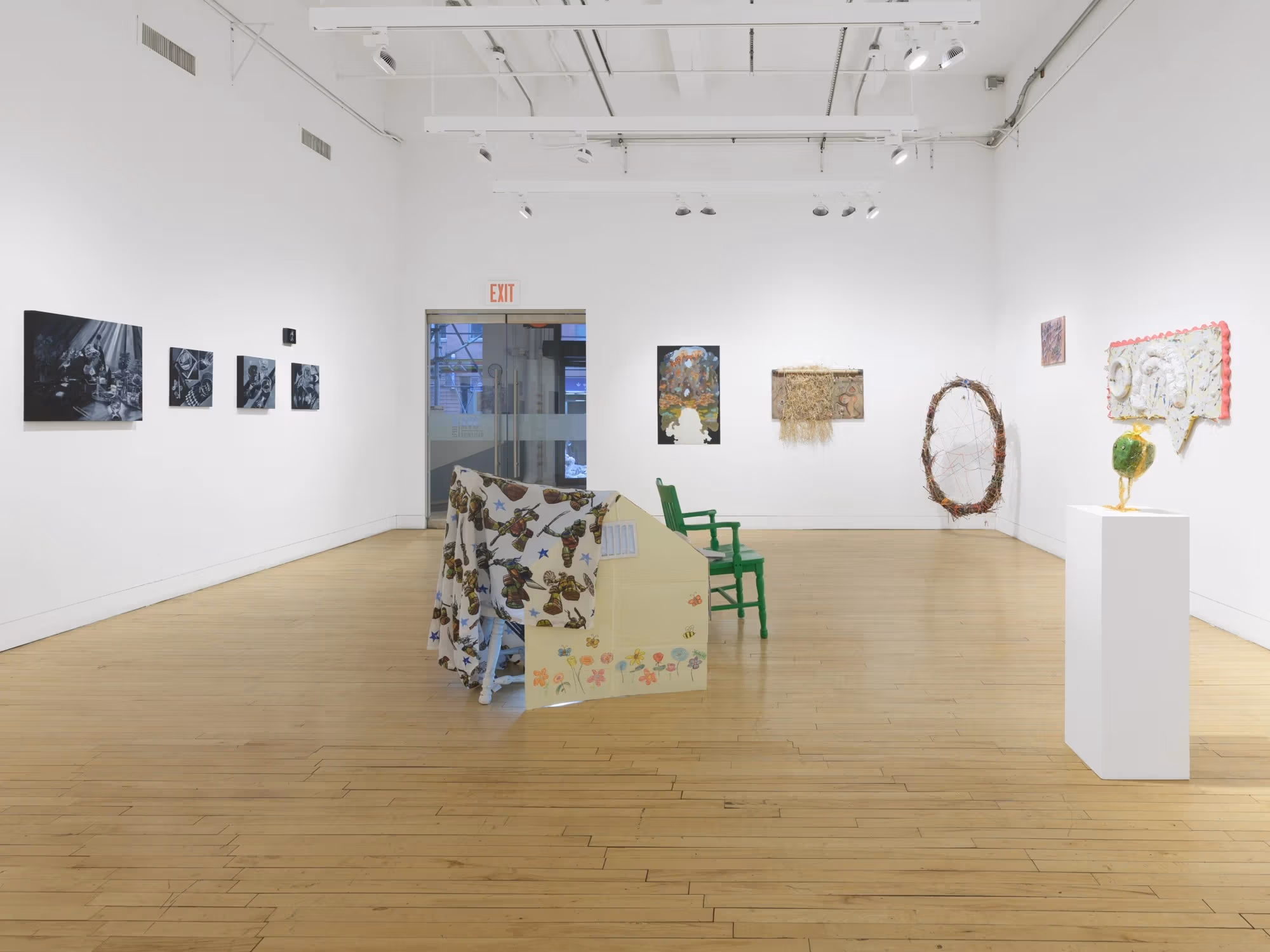 The SVA Flatiron Gallery, with paintings on the left wall, and mixed media artworks on the center and right wall, and a large sculptural piece in the center of the room.