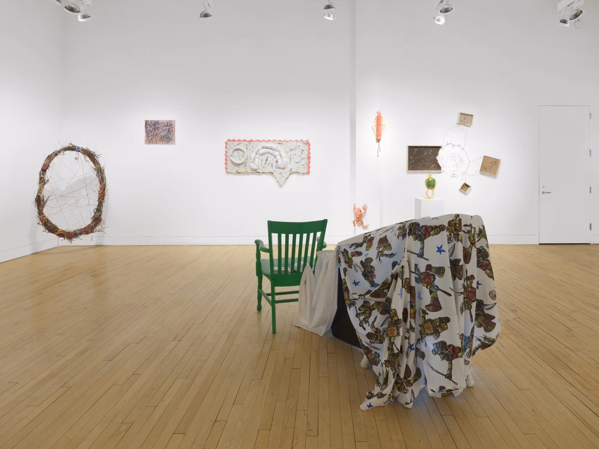 On the far wall is a series of mixed media sculptural artworks hung on the wall, with another large sculptural piece in the foreground.