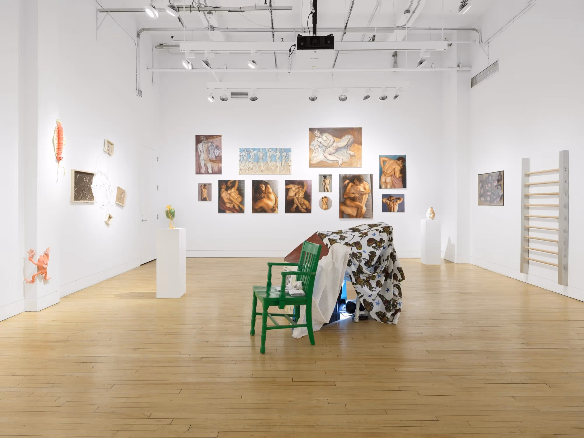 Each wall of the gallery is filled with several different artworks and paintings, and in the center is a sculptural piece containing a green chair.