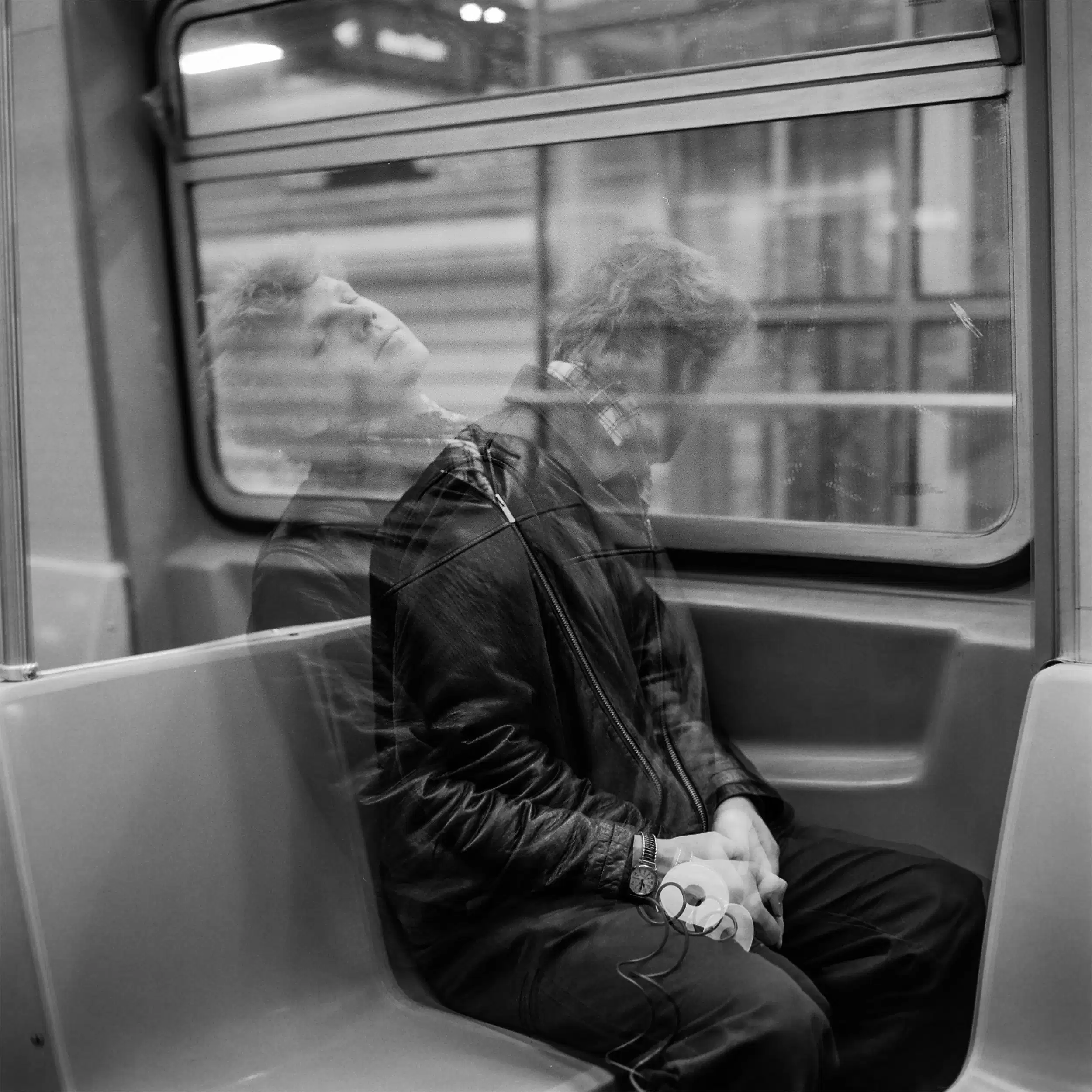 Double exposure black and white image depicting two people sitting inside each other, with their heads leaned away from one another.