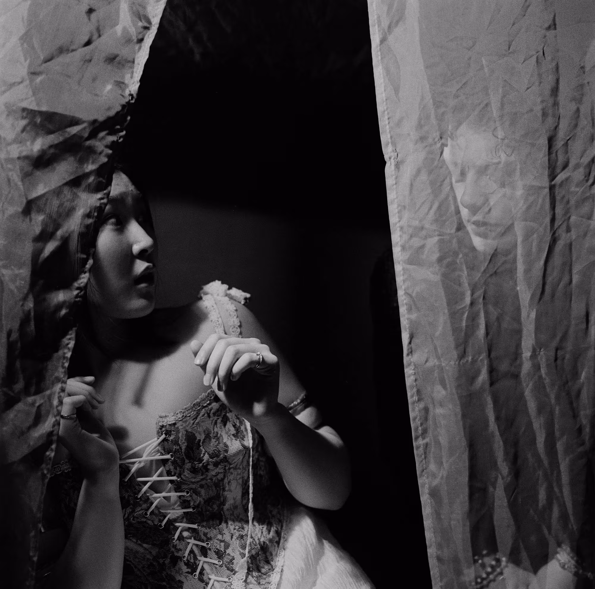 Silver Gelatin Print of a woman surprised by a ghostly face with no eyes behind her curtain.