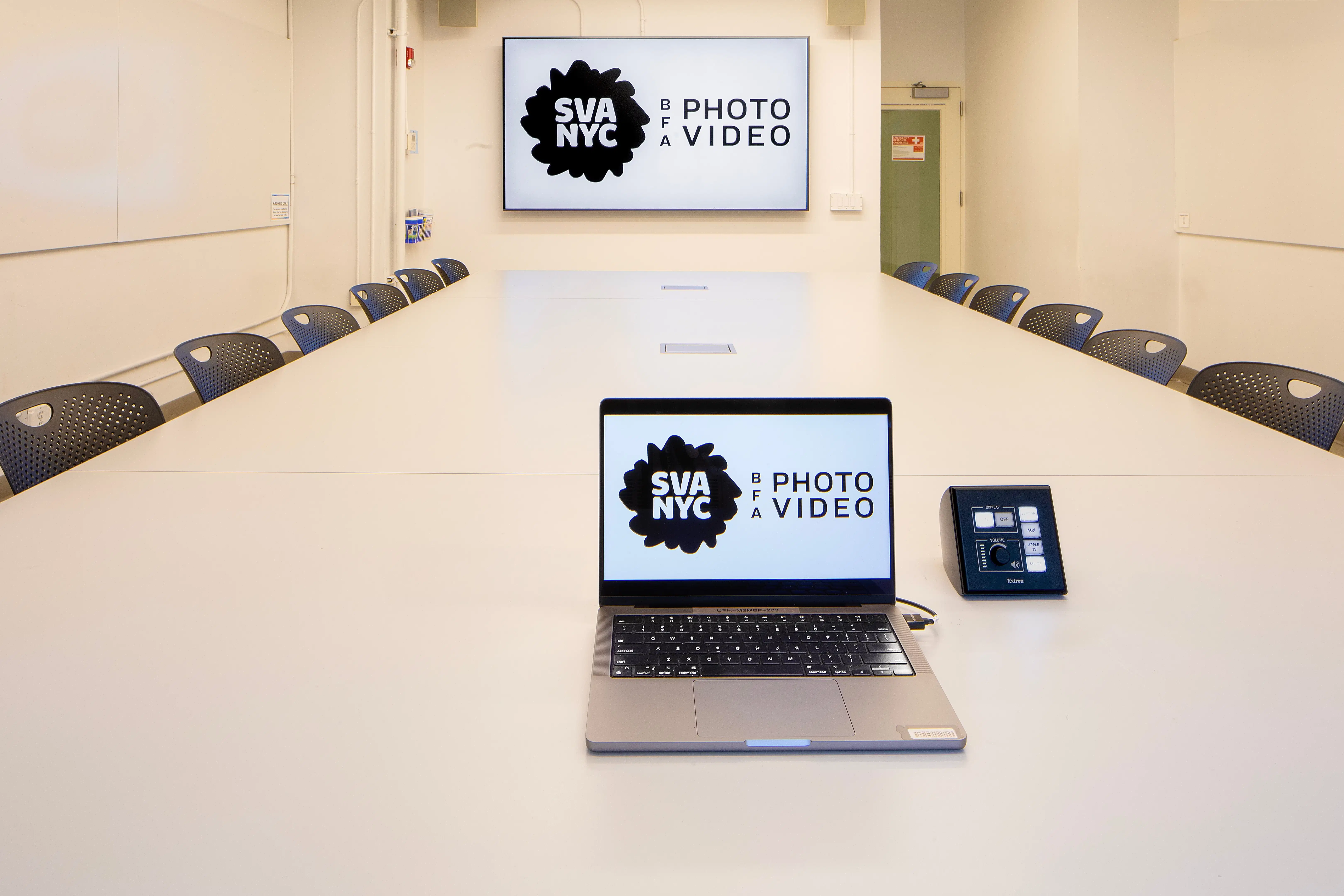 A clean classroom with a large, long table, a giant monitor on the wall and laptop