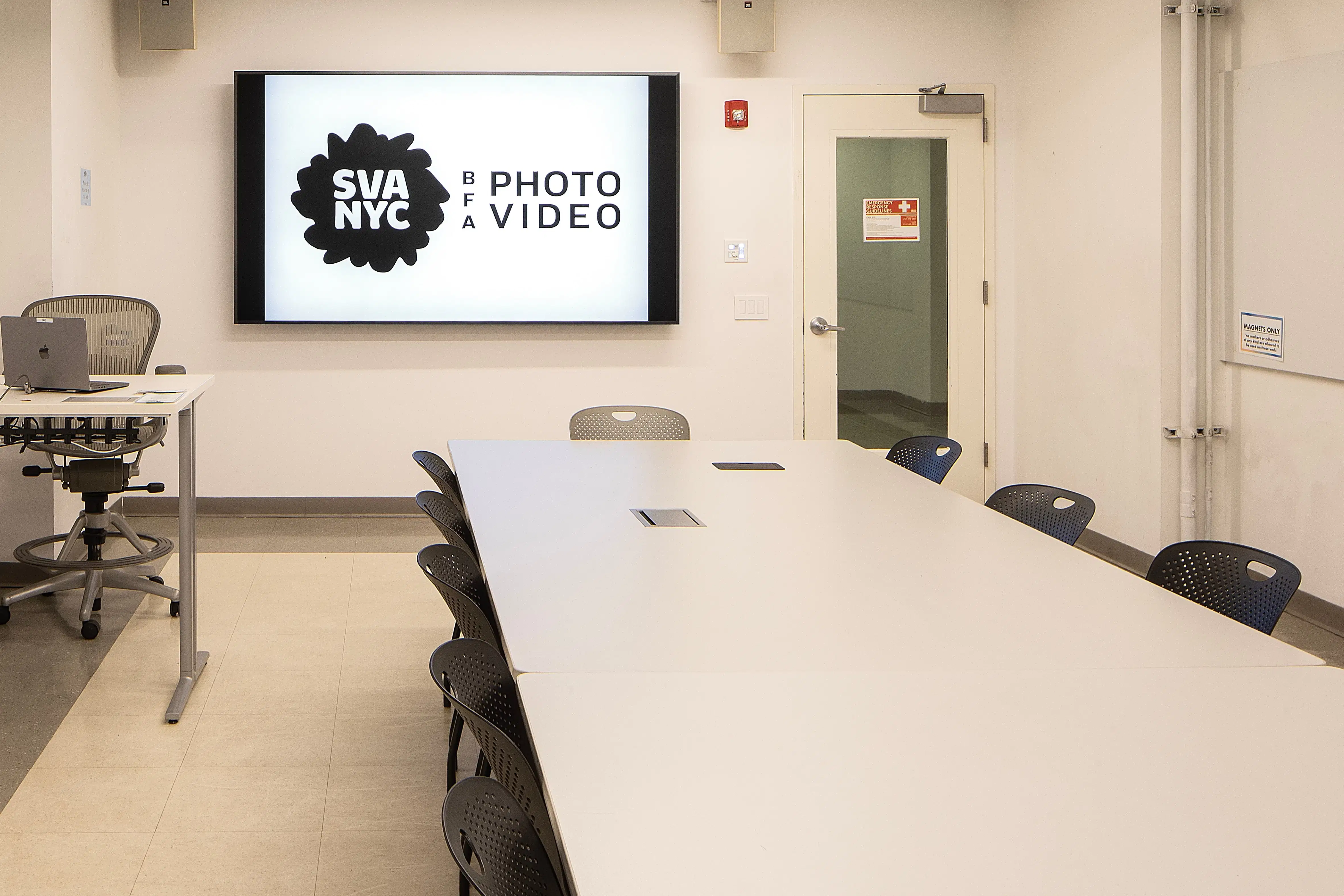 A clean classroom with a long table, large monitor and computer station