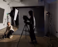 Two people operate camera and sound equipment in a photo studio