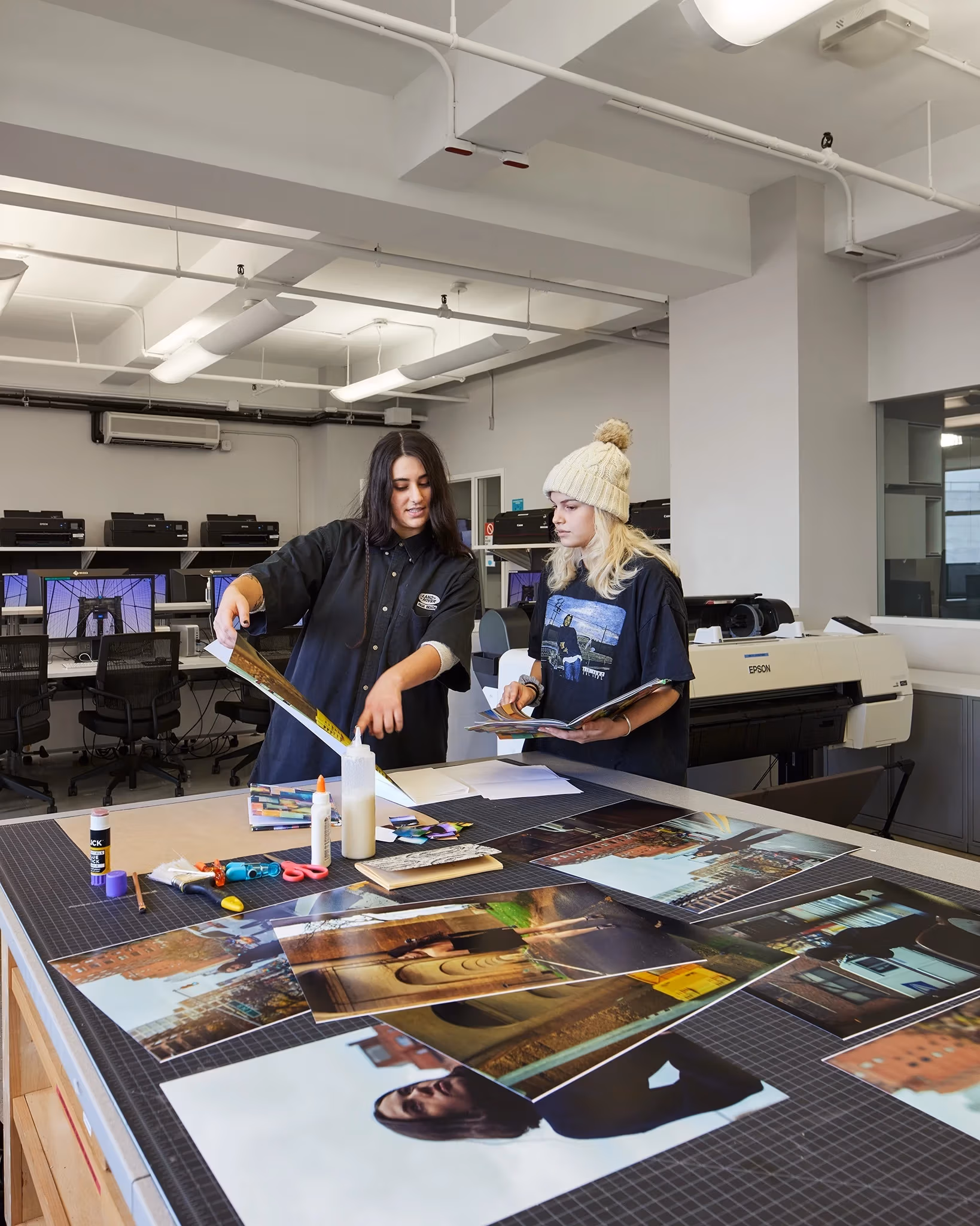 Two people review prints in a digital lab with computers and large digital printers