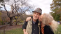 blond woman kisses smiling man on cheek in a park