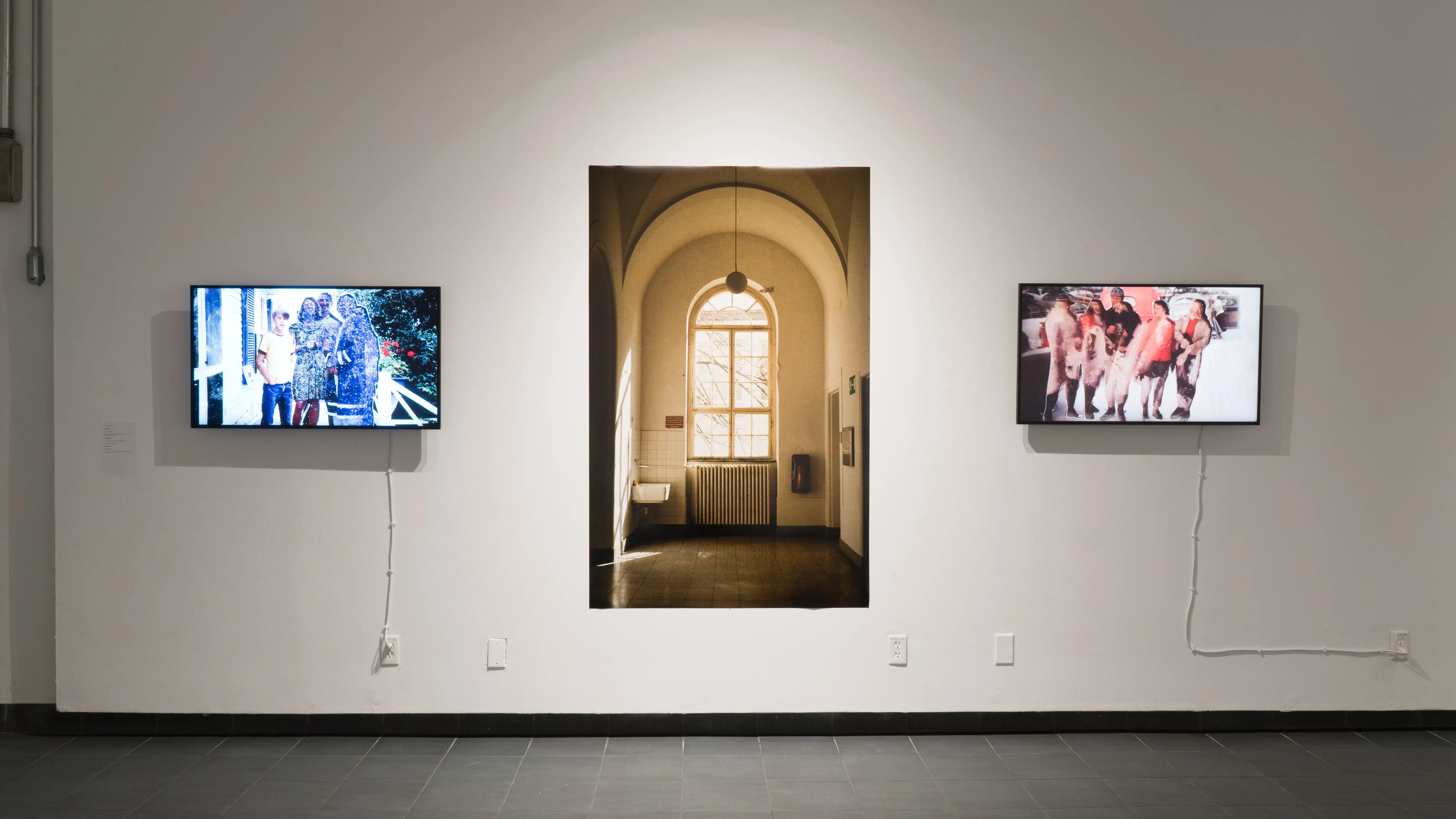 A closer view of one wall in the back gallery, showing a monitor on each side of a large print featuring a window and radiator.