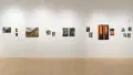 Straight shot of one wall in the Flatiron Gallery, showing multiple prints of industrial moments in varying sizes lining the walls, and an extra large print in orange showing two arches towards the right.