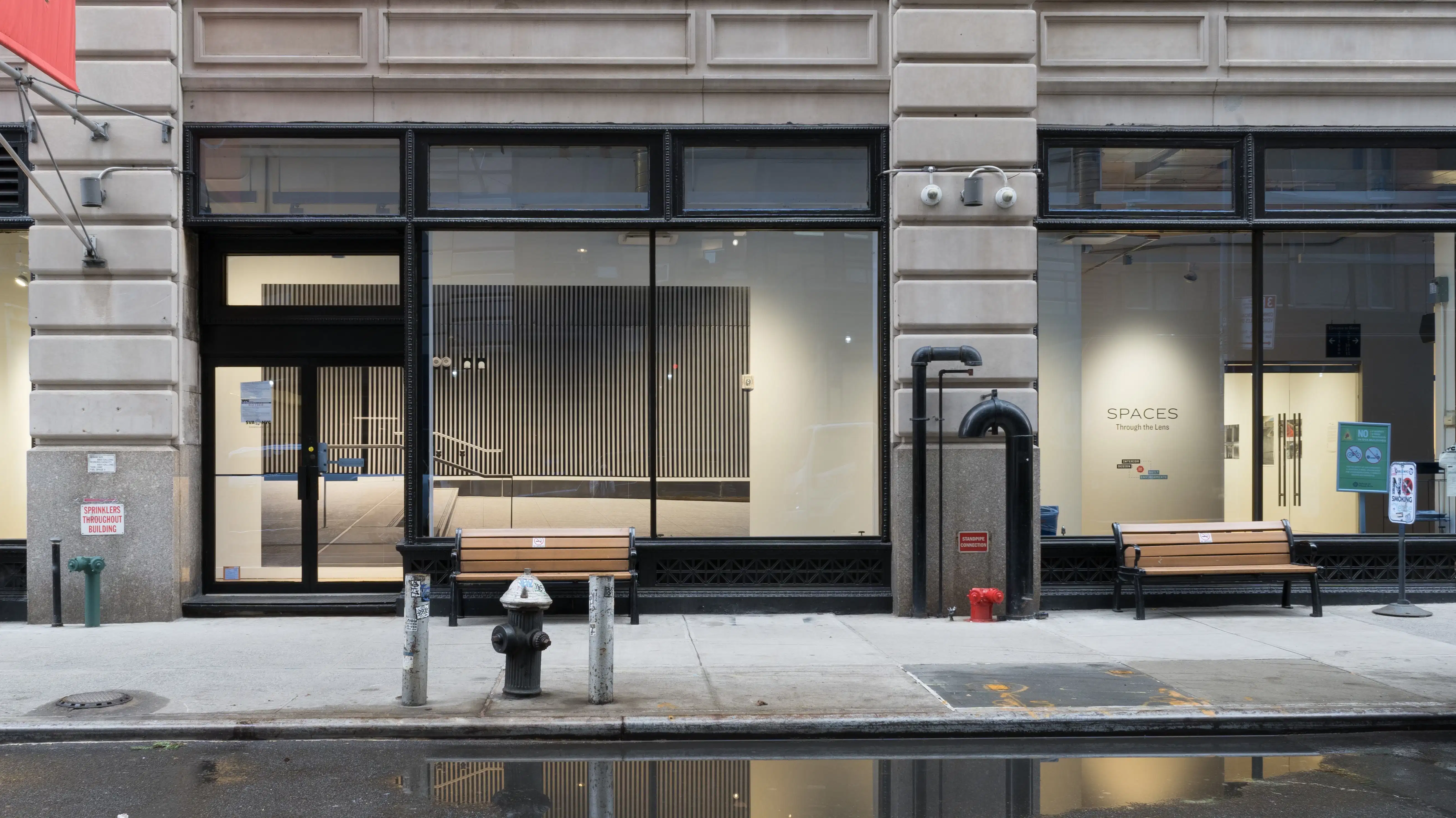 View of the street in front of the Flatiron Gallery, showing the sidewalk and the large windows, with the large vinyl print visible through the windows.