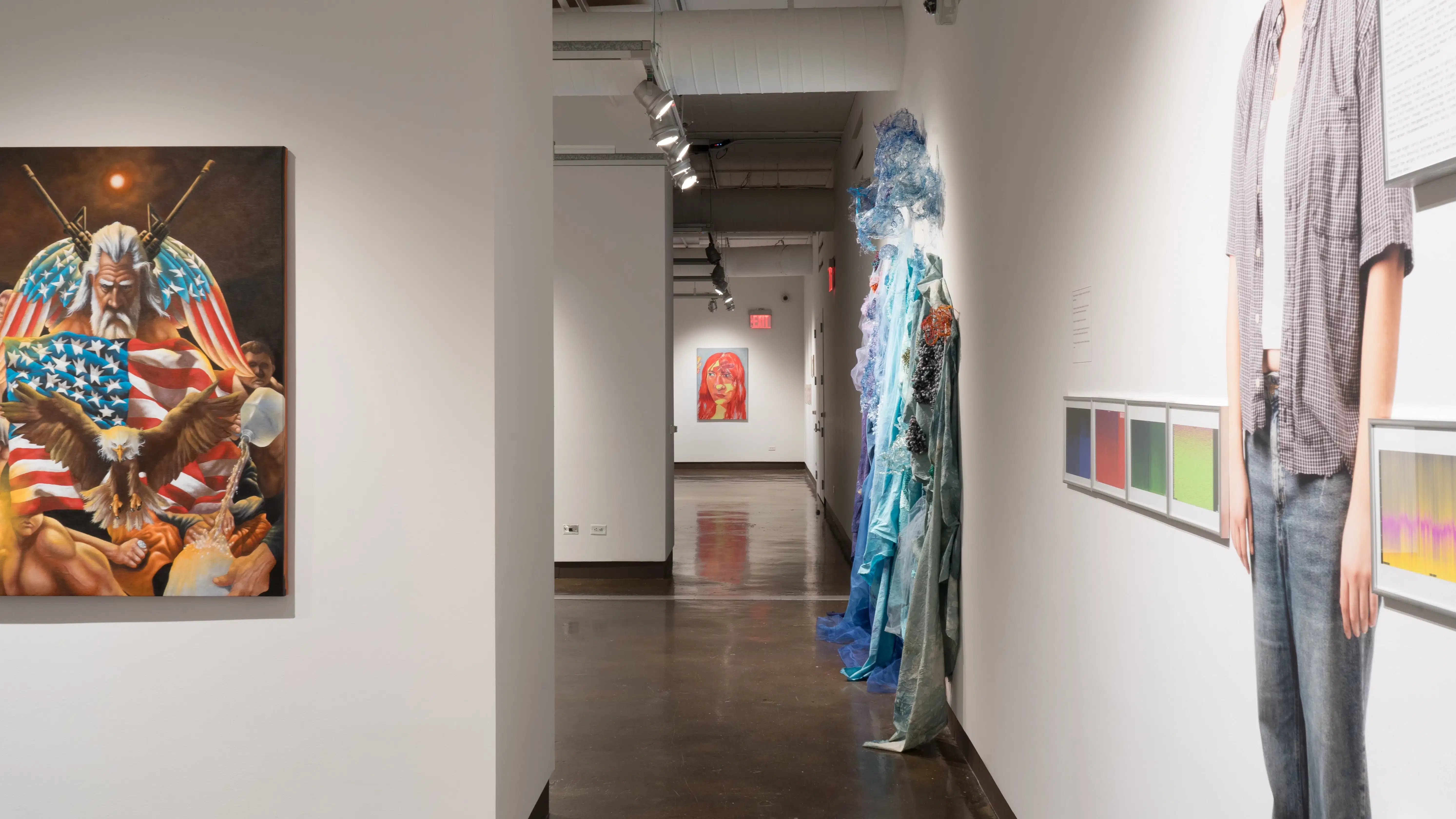 Looking down the right hallway of the SVA Chelsea Gallery, some works from gallery one are still visible. A painting of a woman’s face hangs on the very back wall of gallery four. A mixed-media textile installation hangs on the right side of gallery two.