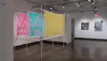 In the gallery four alcove, three colorful sheets of plastic are stretched across a structure of metal poles. Beyond the alcove, two greyish paintings depict scenes of city life.