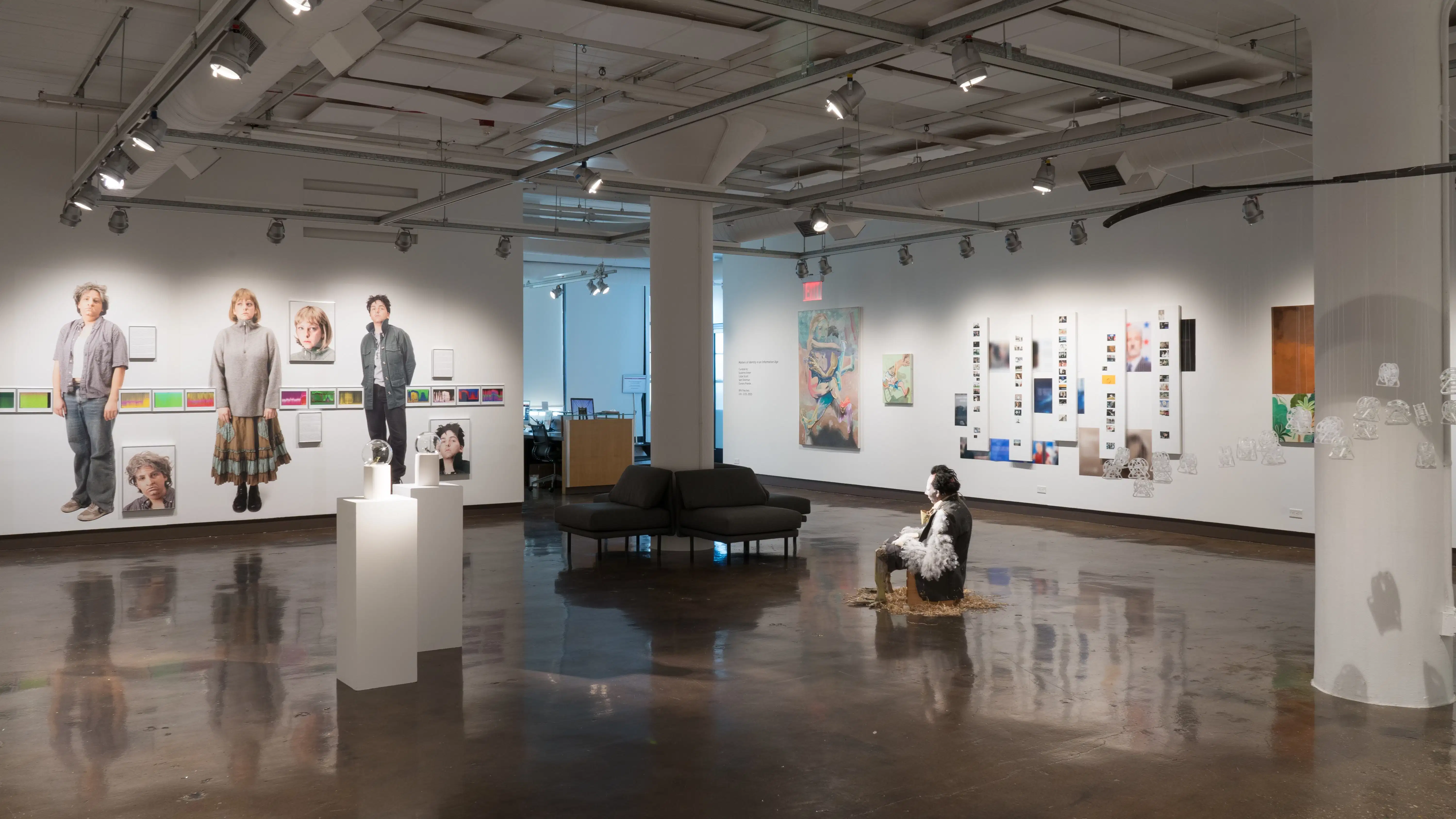 A wide view of gallery one shows a range of photographs, paintings, sculptures, and mixed media works. The gallery’s front desk is visible at the far end of the room.