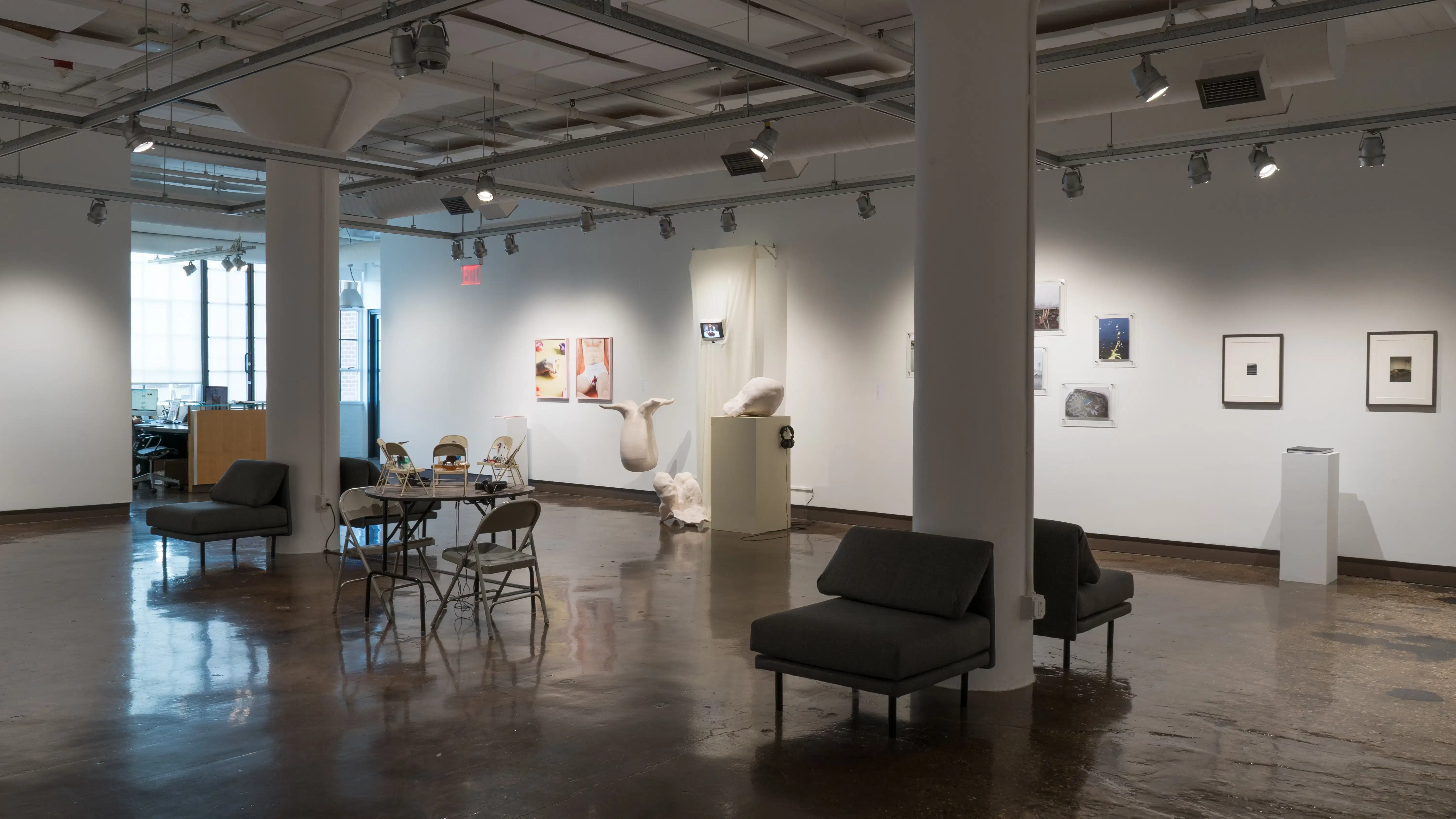 General view of gallery one space, photography based work lines the walls along with installation table pieces in the center of the room. 