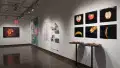 General view of gallery four wall, containing 6 part series of decaying fruit sculpture photographs, along with the sculptures resting on two tables below. Further down are various works containing large scale prints, including shelves with small scale photographs. 