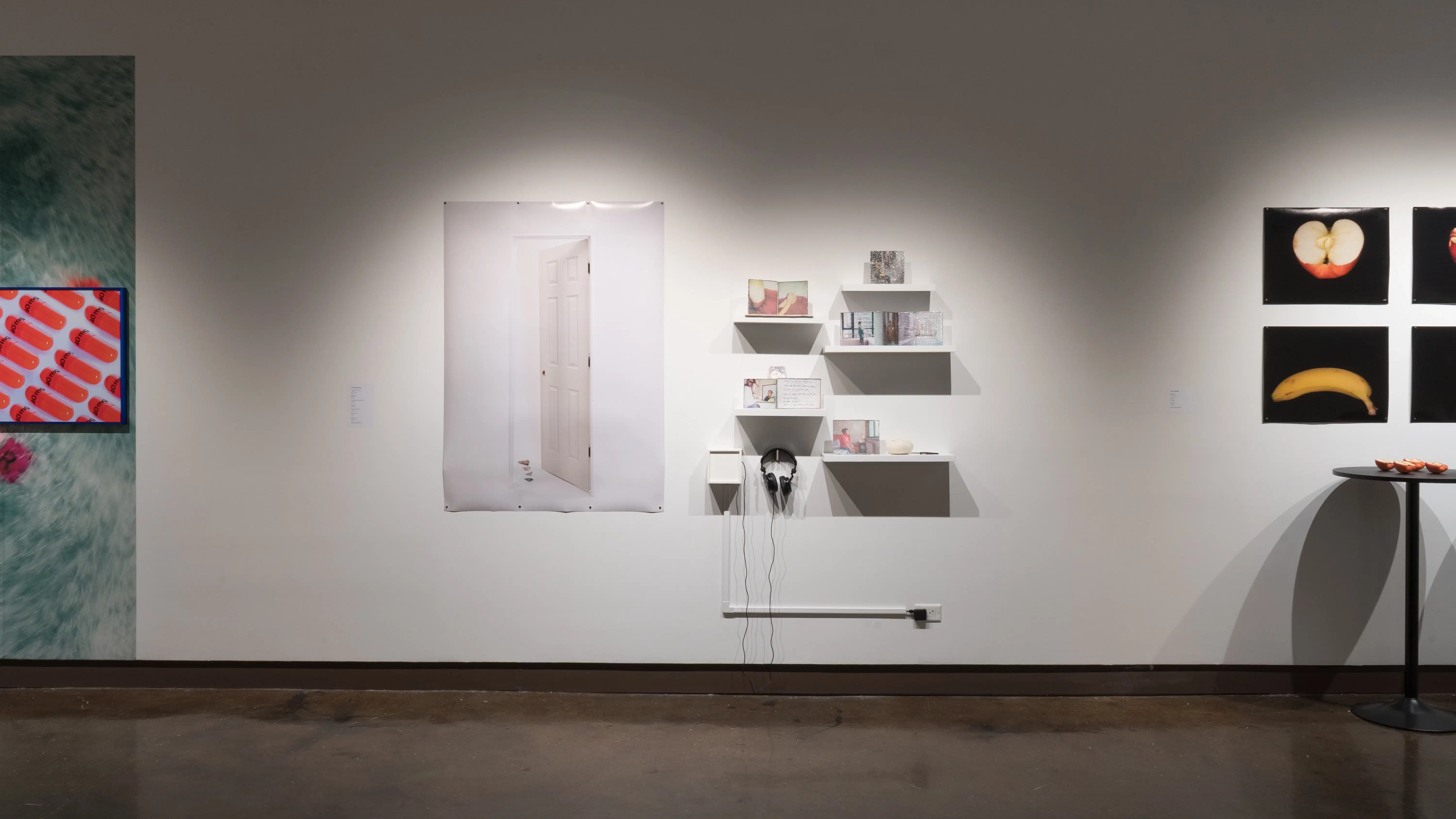 One large scale print of an opening door next to several small white shelves consisting of small scale photographs, letters, and found objects, a headset is below.