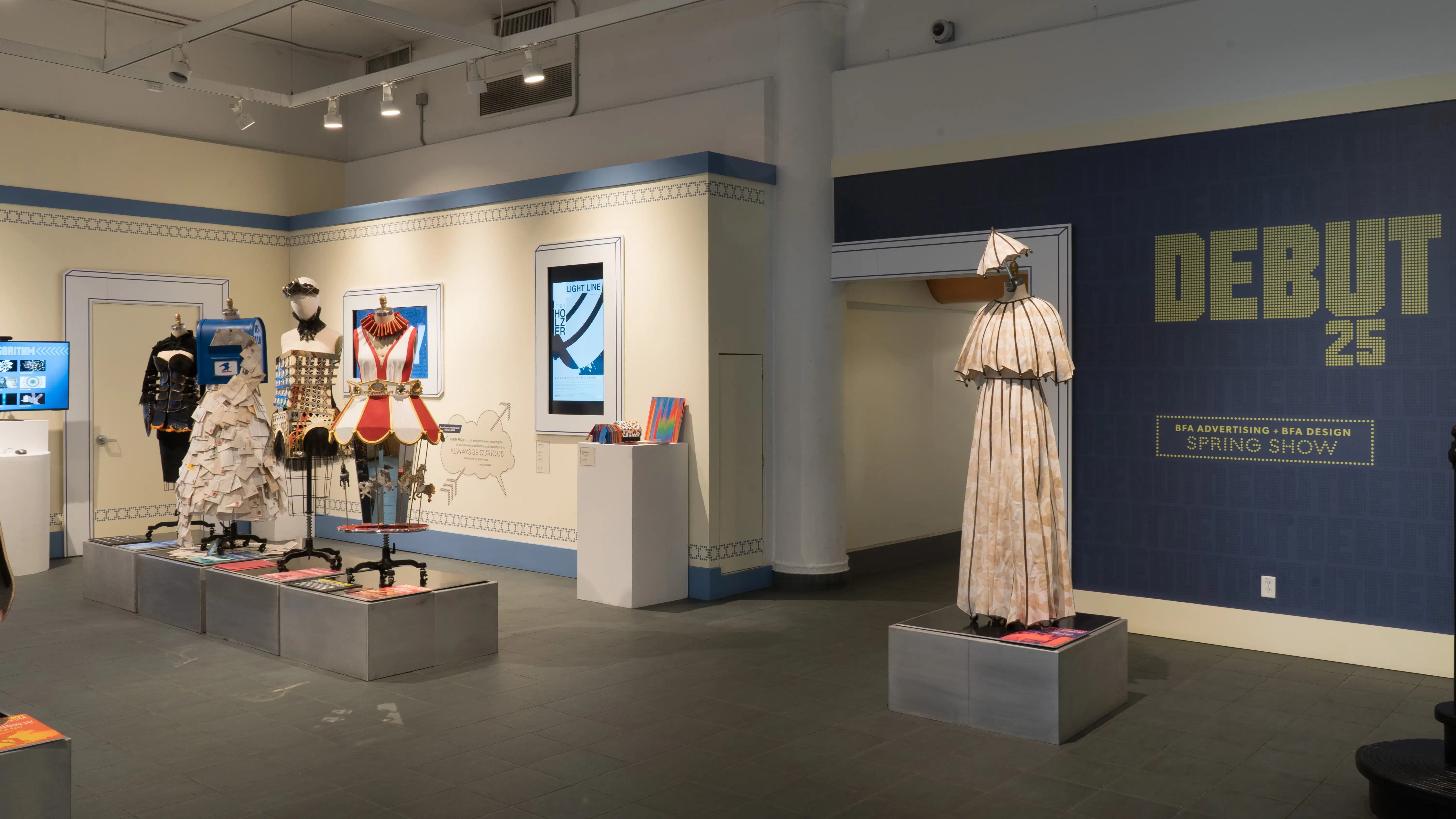 The five total mannequins dressed in costumes inspired by various items are on display in the lobby area. Behind one mannequin the wall vinyl reads “Debut 25: BFA Advertising, BFA Design Spring Show.”