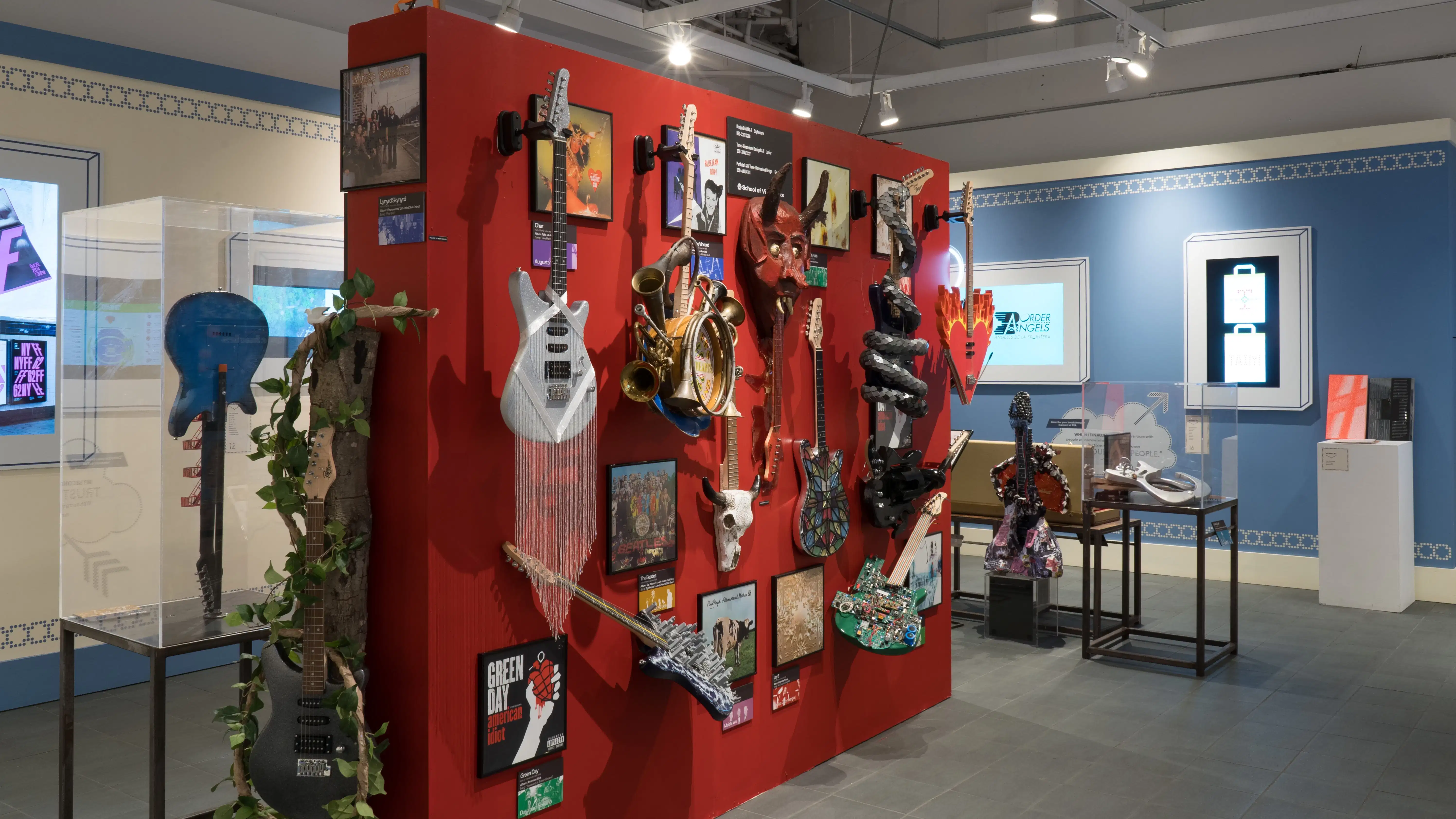 A red wall in the center of the room displays many guitars with various designs for their bodies, like snakes and stained glass windows. On the surrounding walls, design and advertising projects play on monitors.