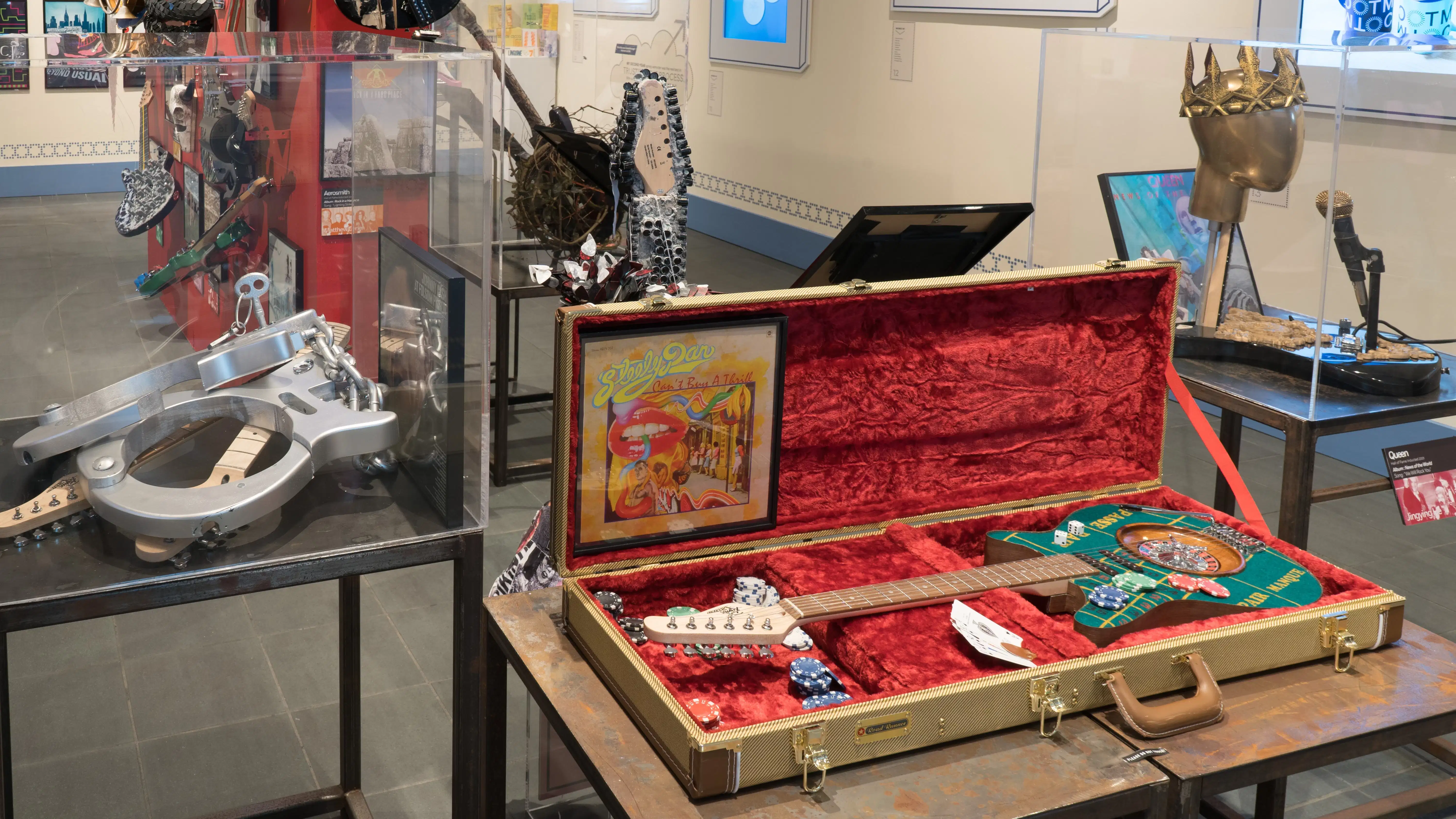 More unique guitars are displayed on pedestals grouped on one side of the room. In an open red-lined guitar case, one guitar resembles a roulette table.