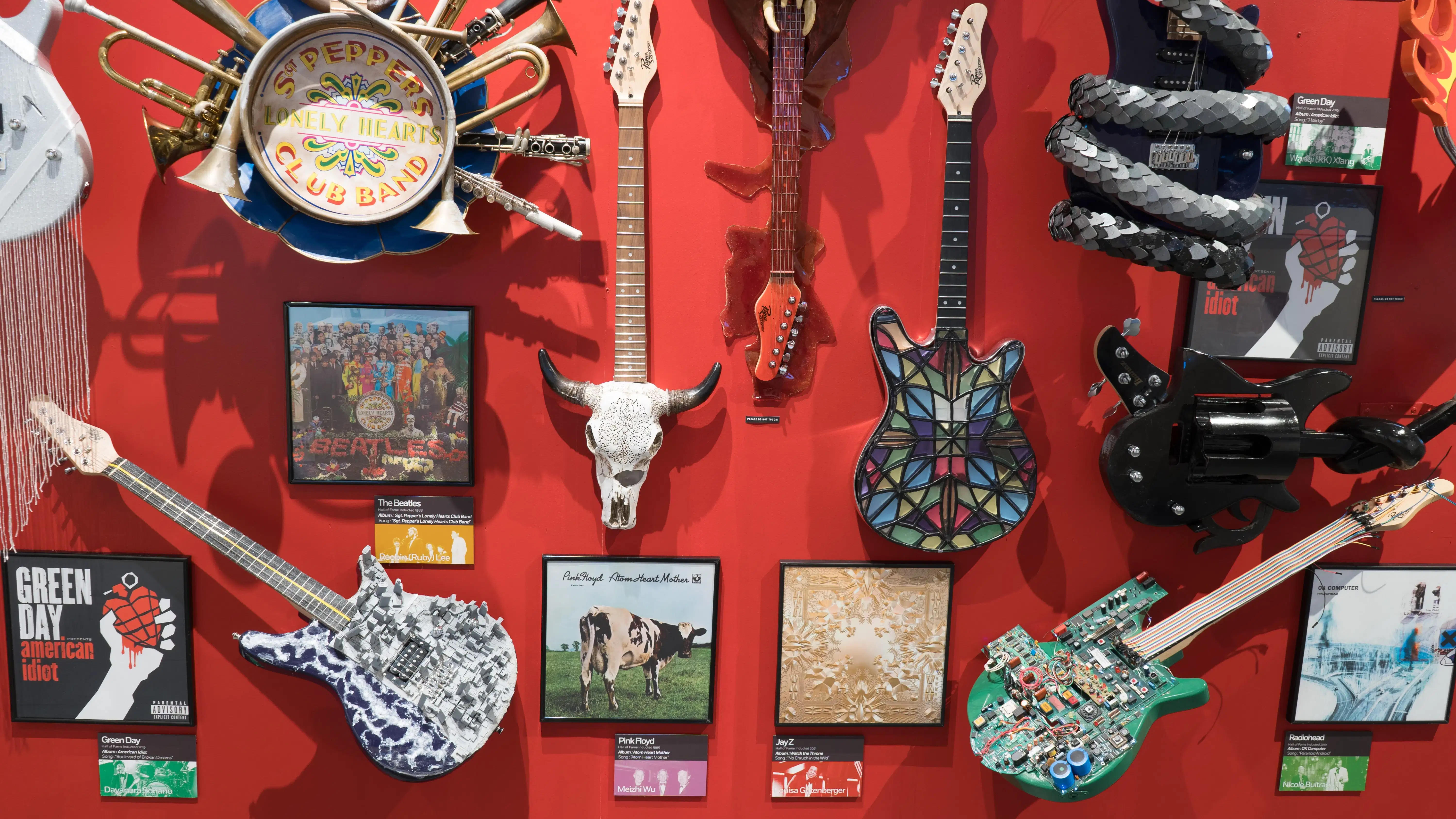 Looking closer at the red wall full of guitars, we see guitars inspired by albums from Green Day, The Beatles, Pink Floyd, Jay-Z, and Radiohead.