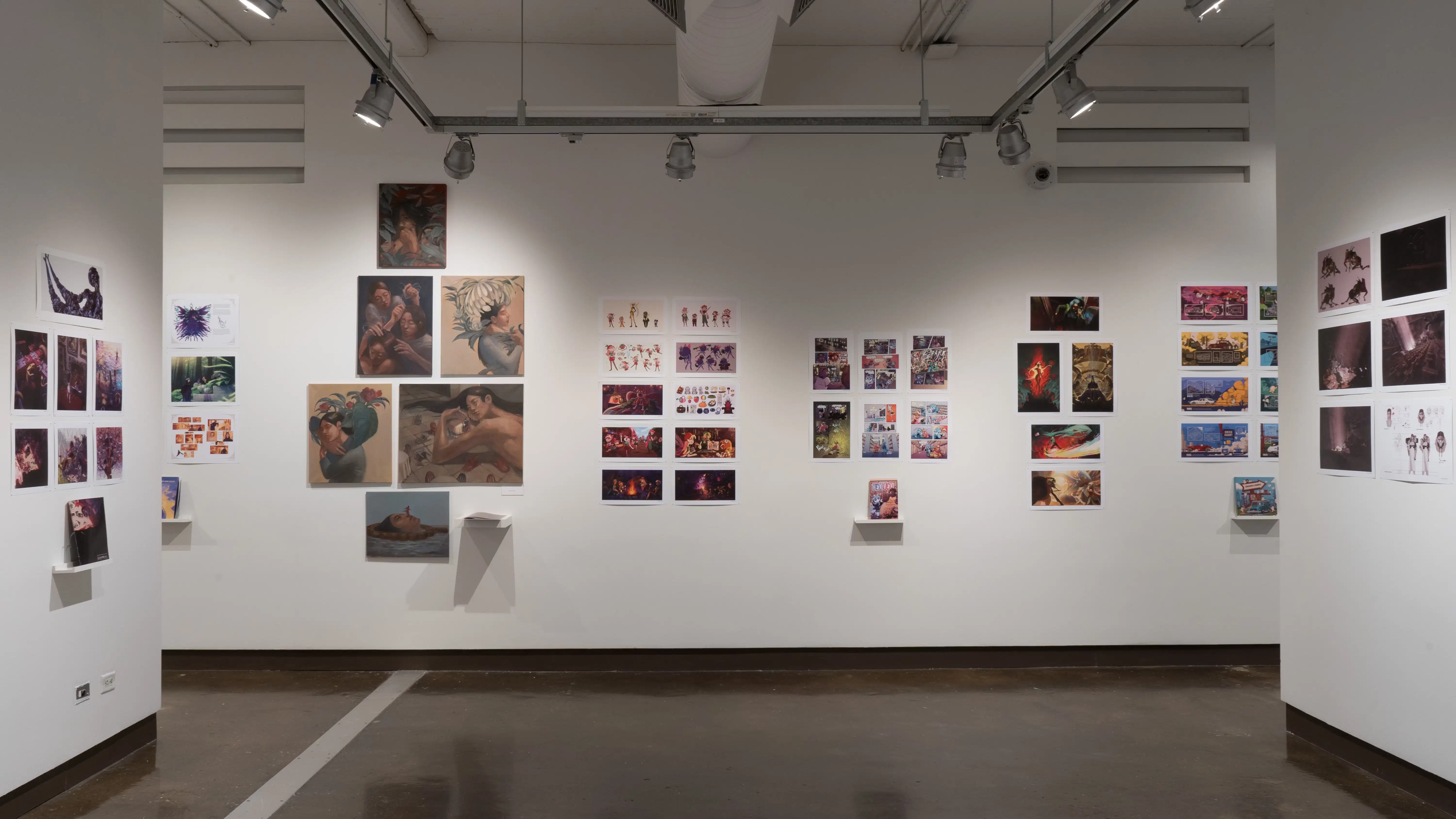 In the second gallery space, three walls are shown. Each wall consists of several horizontal and vertical prints. Some of these prints are accompanied with a personalized book displayed on floating shelves under the prints. On the center wall to the left, there are 6 paintings displayed.