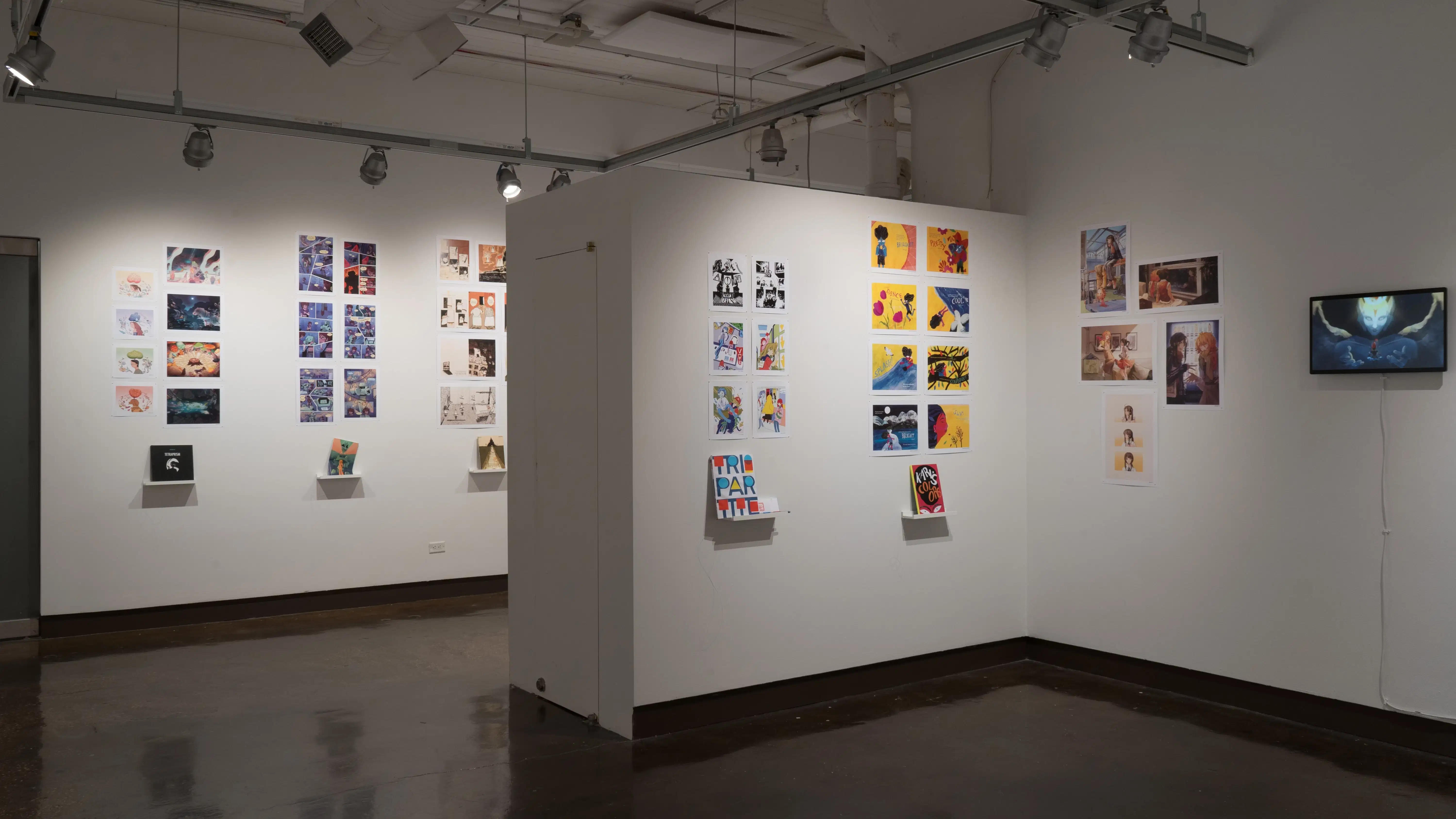 In the first half of the last room of the gallery, several horizontal and vertical prints are displayed on the walls, most accompanied with personalized books displayed on floating shelves under the prints. A monitor is shown with an animation to the right.