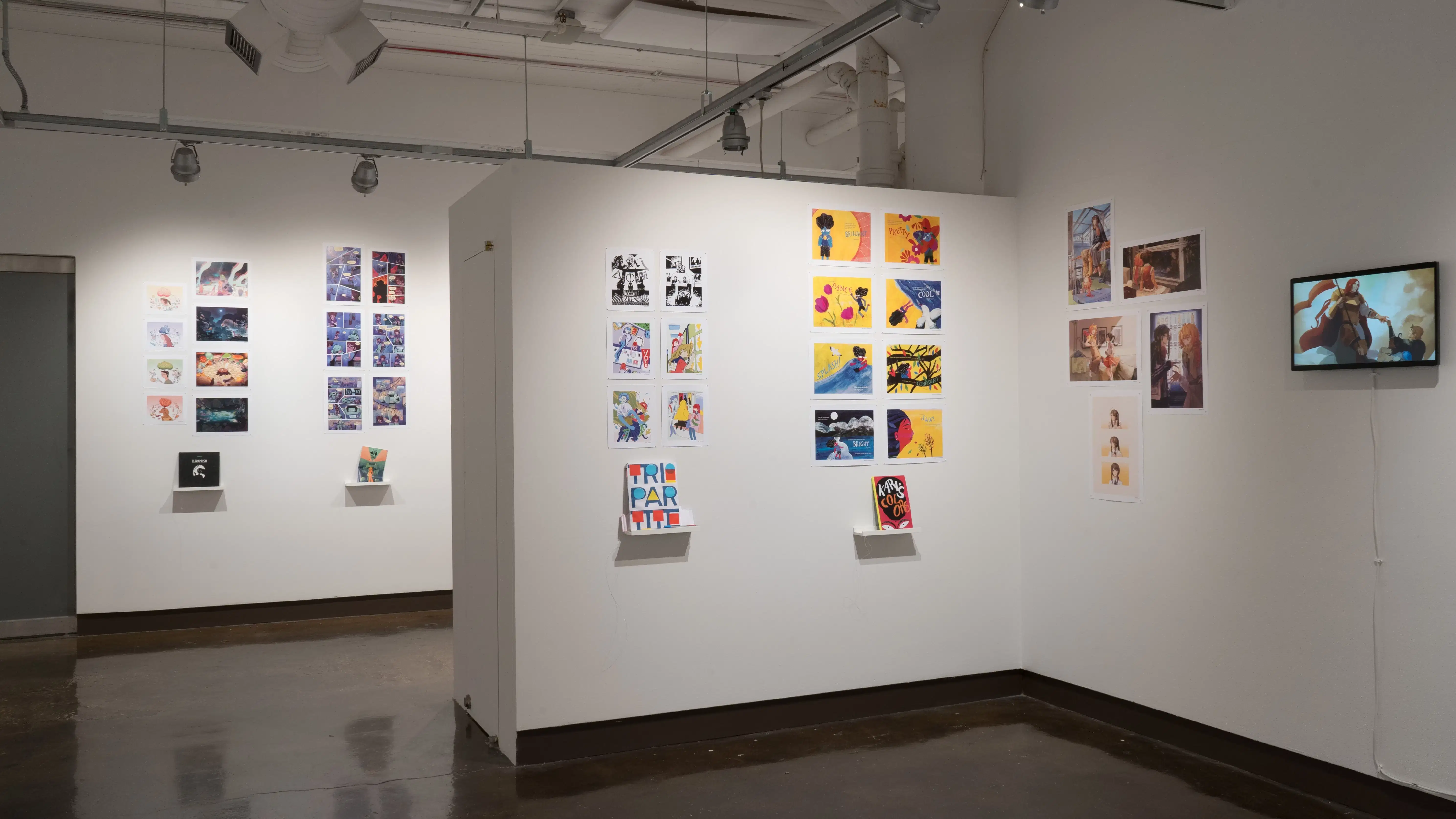 In the first half of the last room of the gallery, there are three walls shown. On the right wall, four prints are displayed. To the right of the prints, a screen displays an animation. On the center wall to the left of the right wall, two groups of prints are displayed with personalized books displayed under the prints on floating shelves. The furthest wall around the corner and behind the main two walls shown displays several horizontal and vertical prints, with books displayed under the two groups of prints.