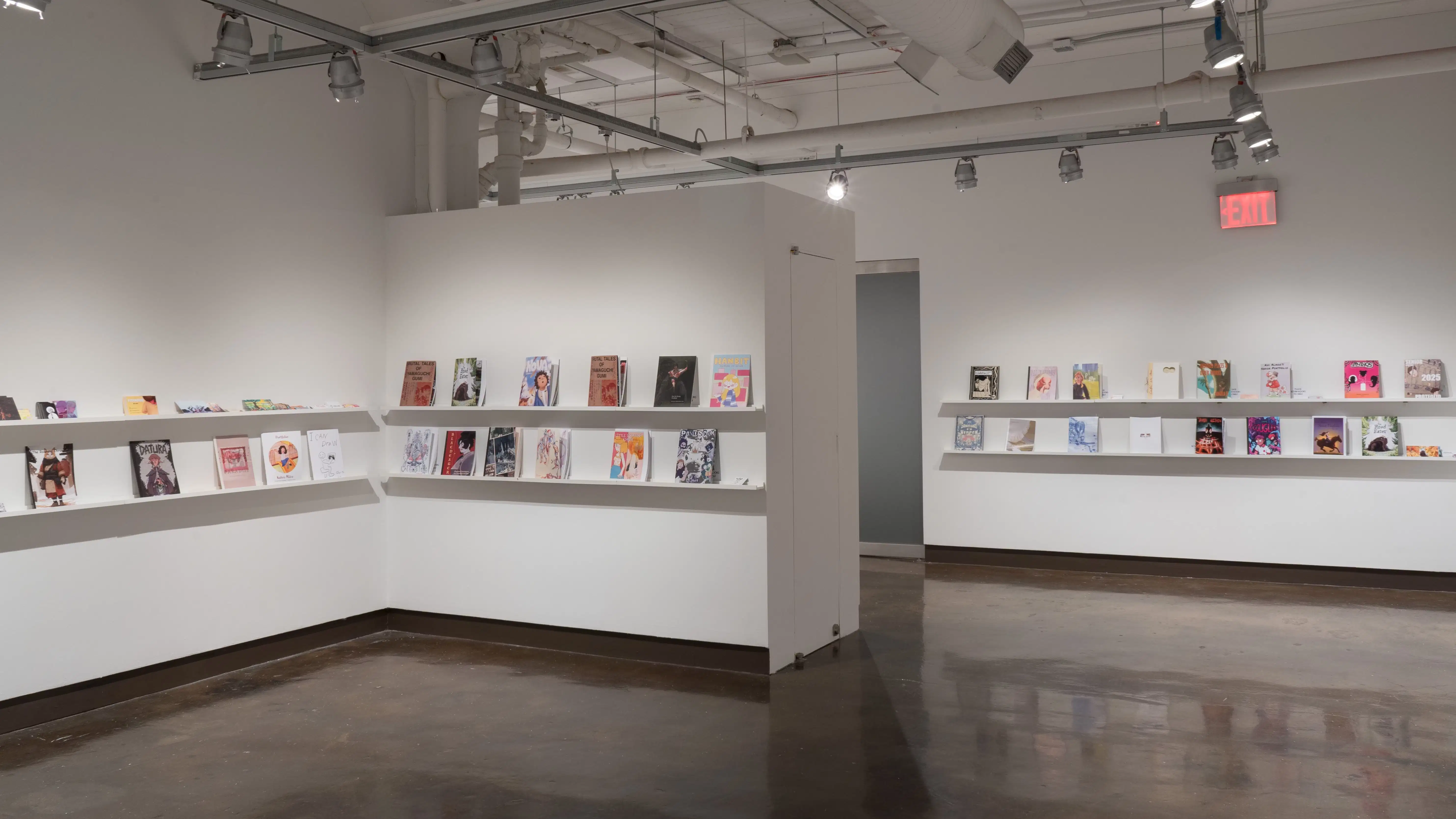 In the last room of the gallery, three walls are photographed. Each wall consists of two long shelves, with each shelf displaying books and business cards.