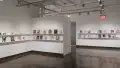 In the last room of the gallery, three walls are photographed. Each wall consists of two long shelves, with each shelf displaying books and business cards. 