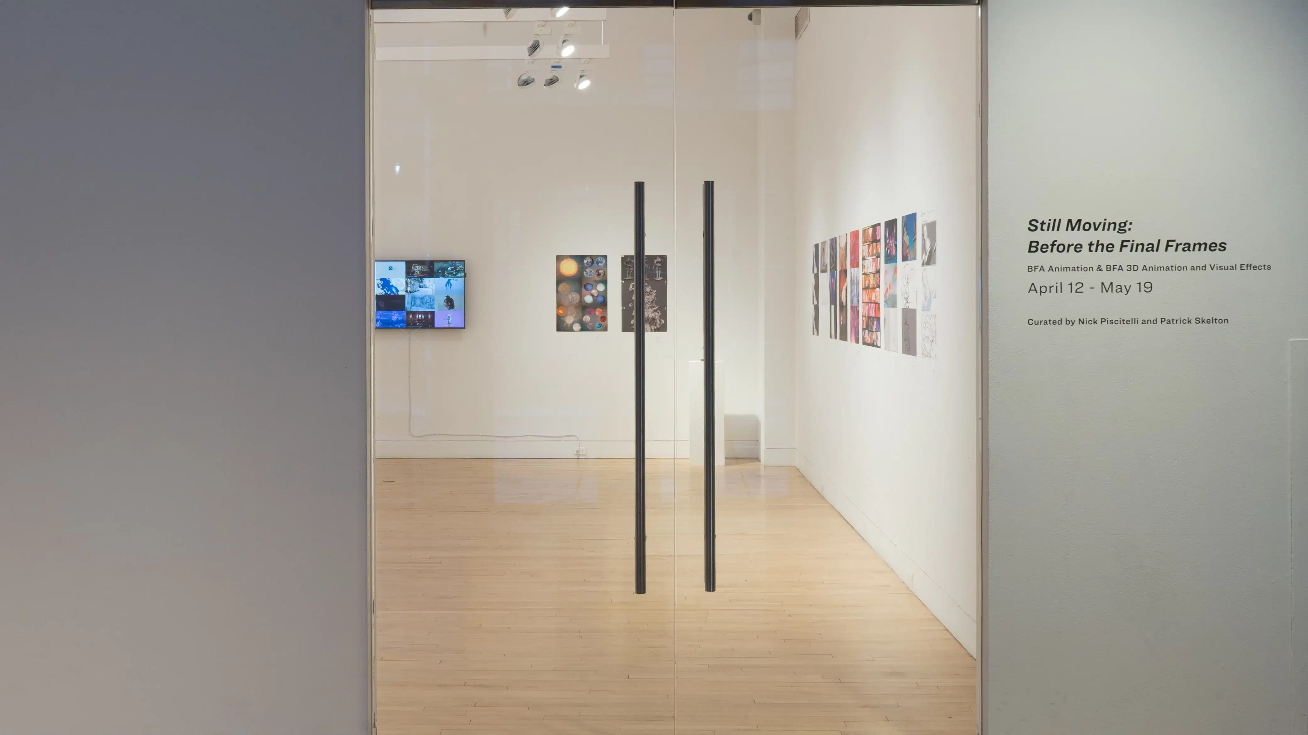 A view of the glass gallery doors at the SVA Flatiron Gallery, with the title to the right in vinyl, and multiple prints and a monitor visible through the glass.