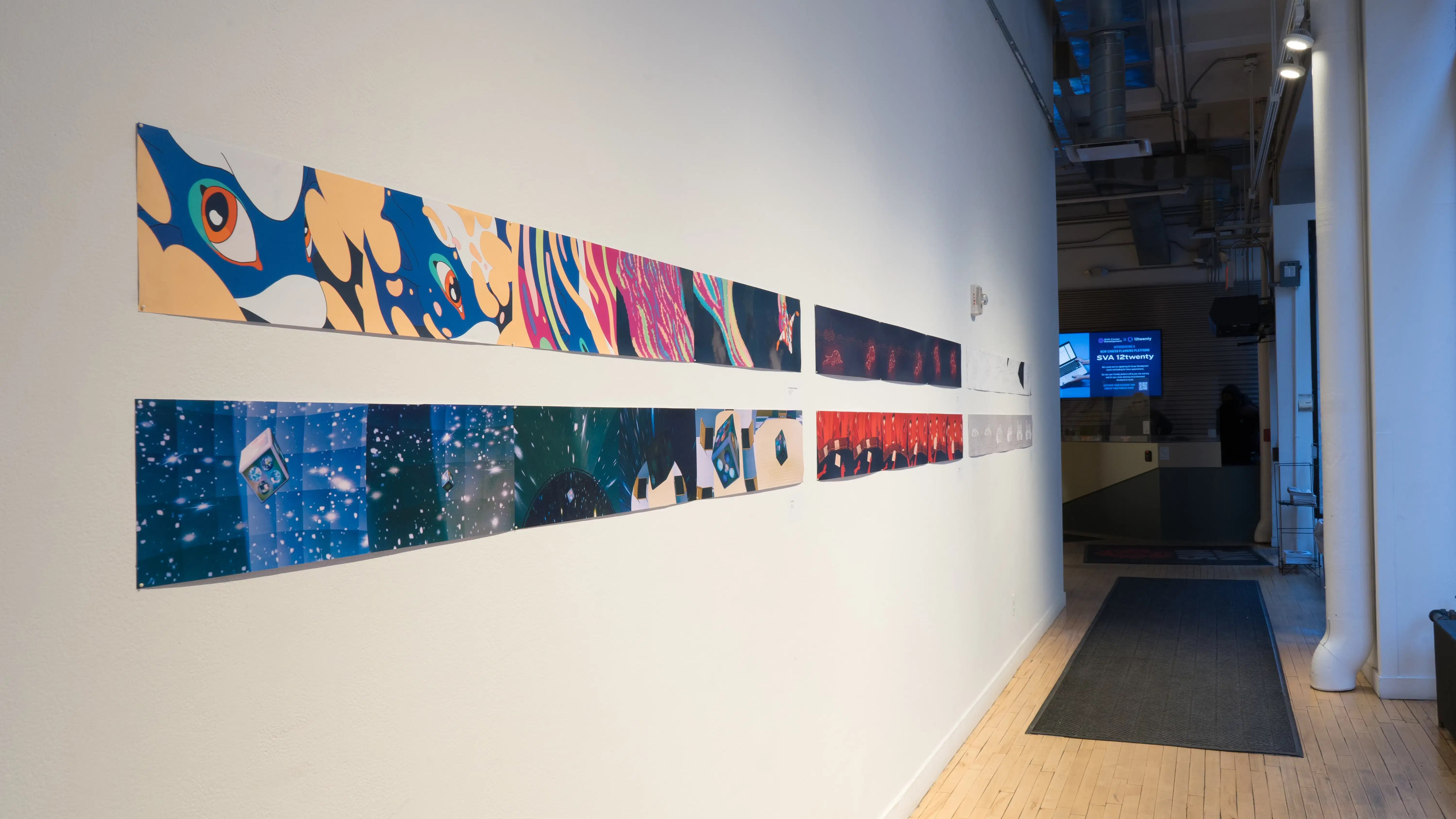 An angled shot of the SVA Flatiron Gallery Windows looking east, showing many colorful prints by BFA Animation students pinned up. A monitor plays reels over the security desk in the far background.