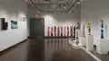 On the far wall in gallery two, narrow, vertical paintings that look like raw meat are hung in a row. On the left wall are the paintings that seem to be cut from a whole, and on the right are several pedestals displaying ceramic sculptures of objects stacked precariously high.