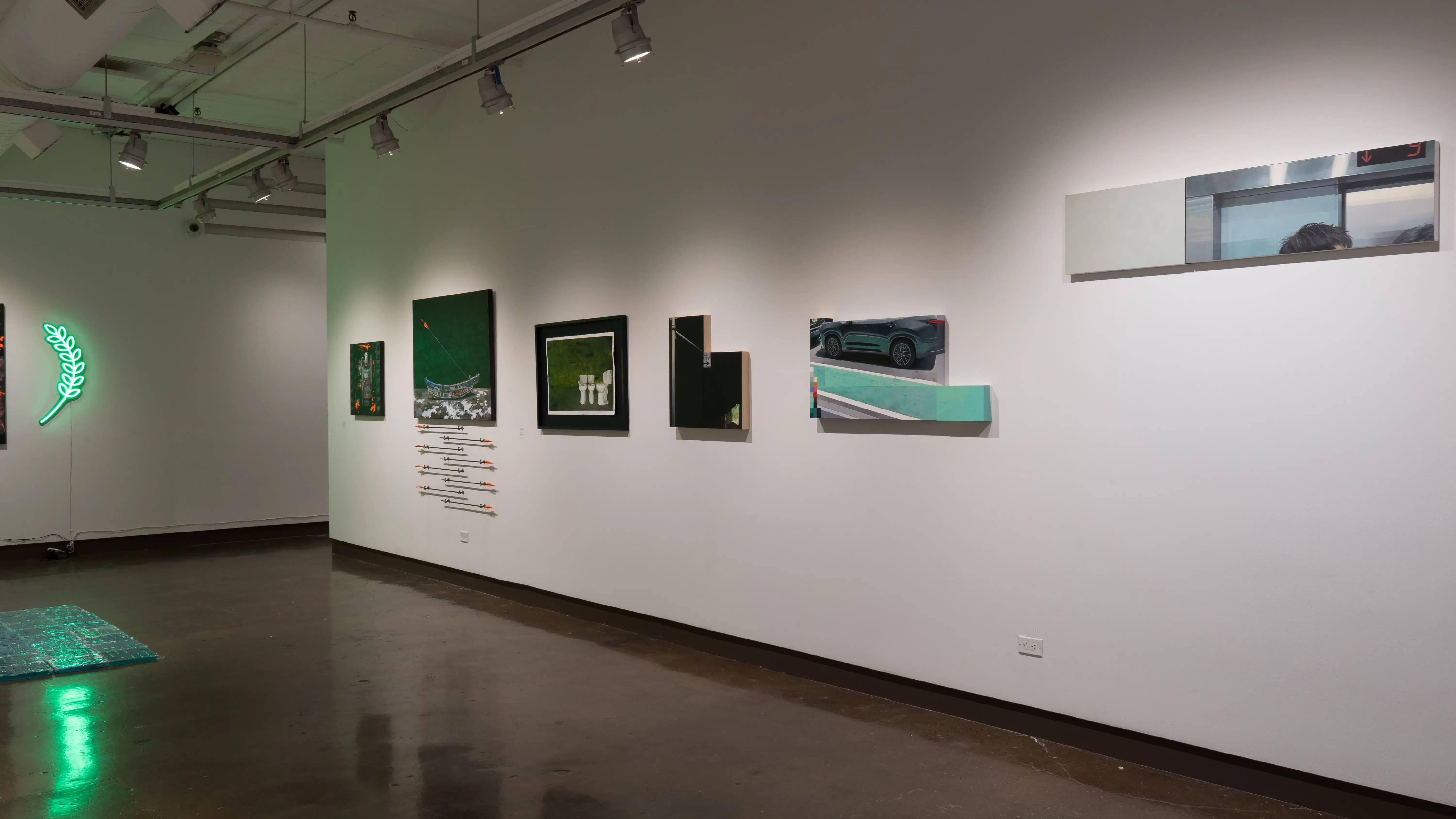 Along one wall of gallery two, paintings on geometric-shaped panels look as if part of a picture has been selected from a larger whole. Beyond them, a painting of a canoe hangs above a set of arrows mounted on the wall.