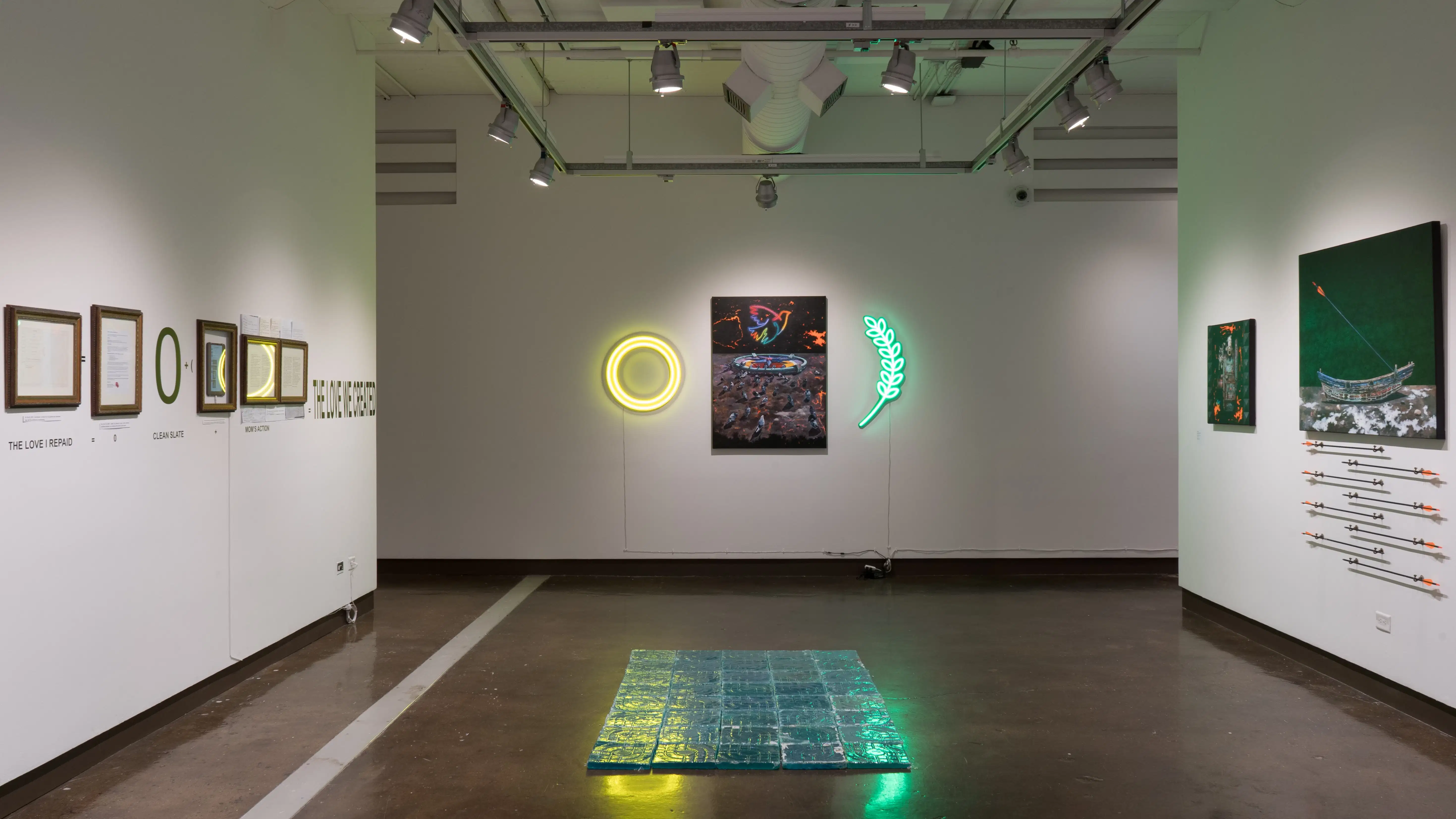 On the far wall in gallery two, a painting of pigeons in a space-like environment hangs between two neon lights. The yellow and green lights reflect on blue, textured resin tiles that have been arranged on the floor. Framed works hang on the left wall, and canvas paintings hang on the right.