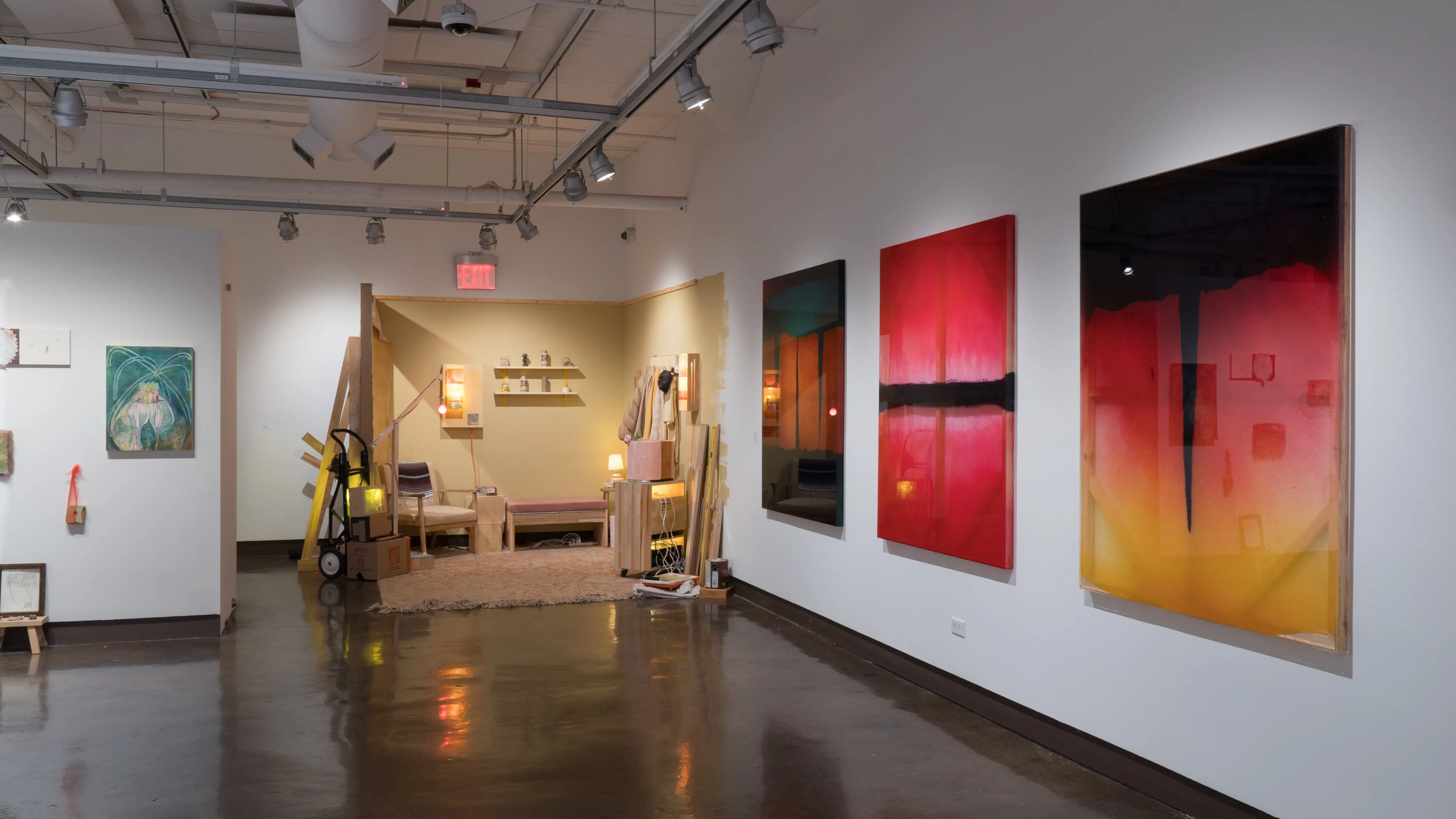 Part of the alcove in gallery four is visible, showing the mixed media panels. To the right, the room installation is set up in the corner, and the large plexiglass paintings hang on the wall beside it.
