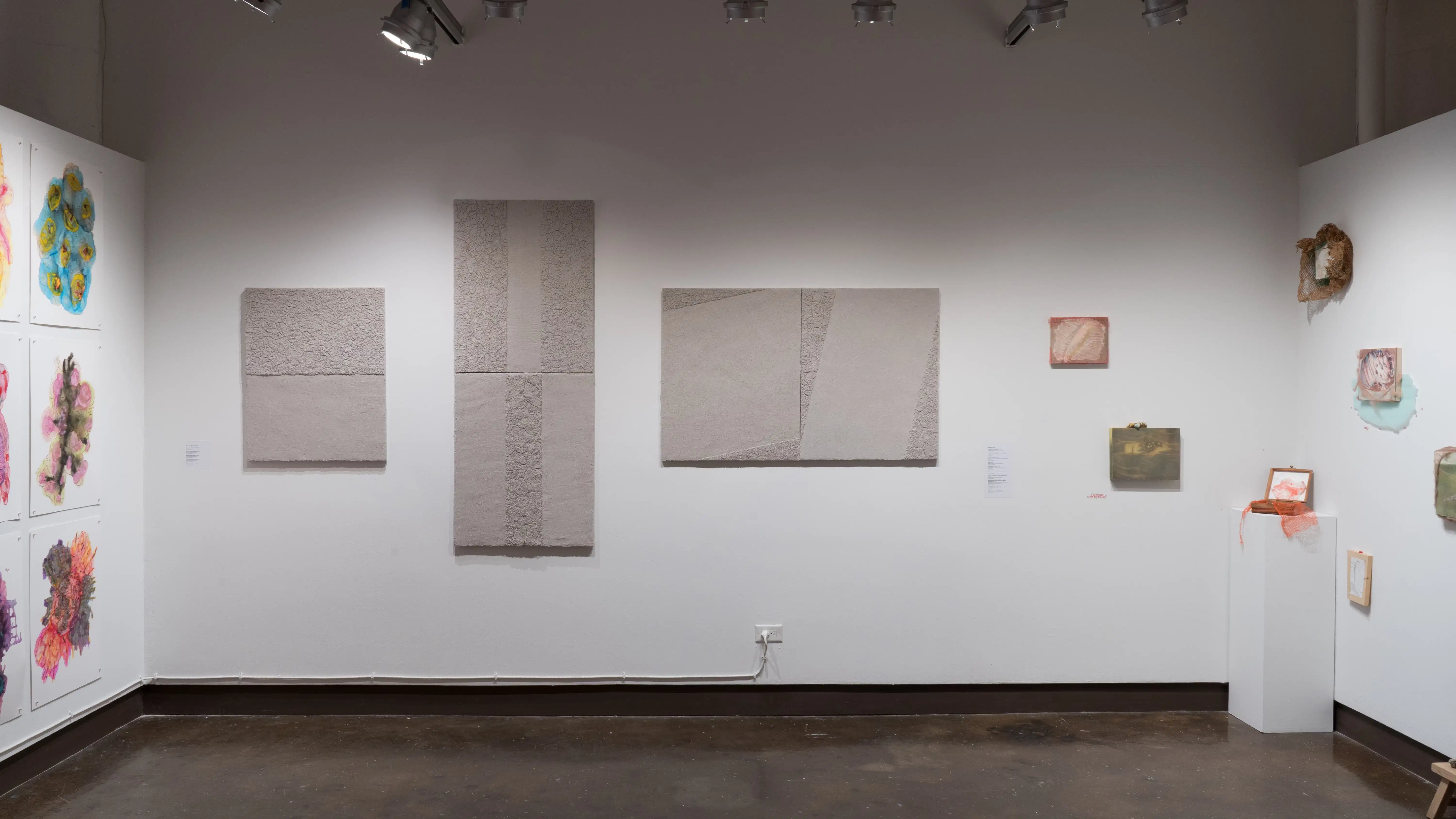 Facing the gallery four alcove, the bright watercolor works, the cement block pieces, and the mixed media panels are all on display.