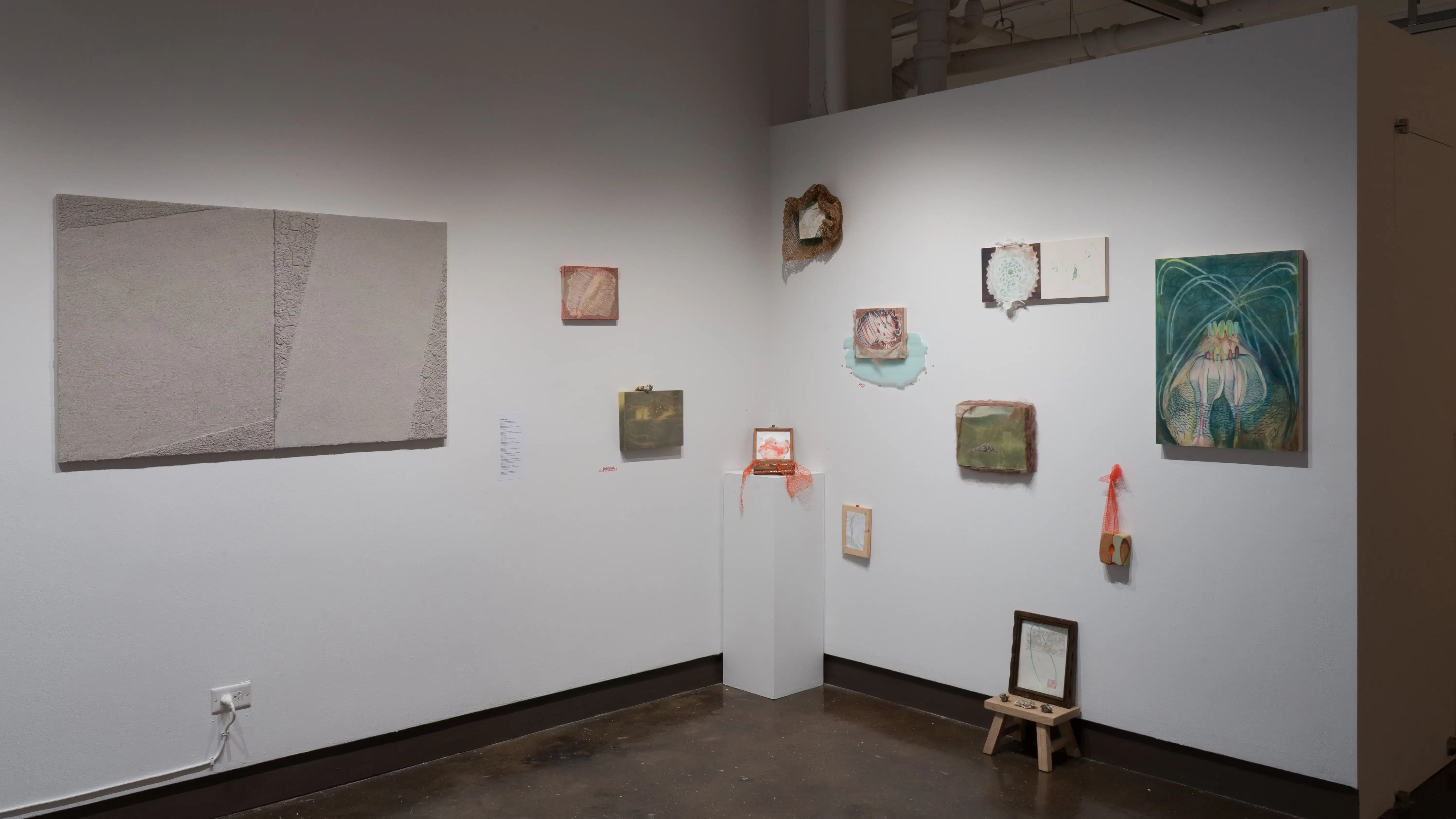 To the other side of the cement blocks, several mixed media works on small to medium panels are arranged in a constellation-like pattern. They feature earthy tones like turquoise, sage green, and clay red.