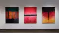 Three large paintings on plexiglass hang in a row on the back wall of gallery four. The paintings evoke a cat eye, using warm, washy colors next to sharp, deep black lines.