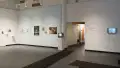 The view from the entrance into the SVA Gramercy Gallery. Two screens display video art, and a light blue wall to the left has a series of photographs on it. There are more photographs on the wall perpendicular to the light blue one.