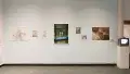 A series of dreamlike images on a light blue wall in the gallery lobby. To the right of the photographs is a small box television playing a video.