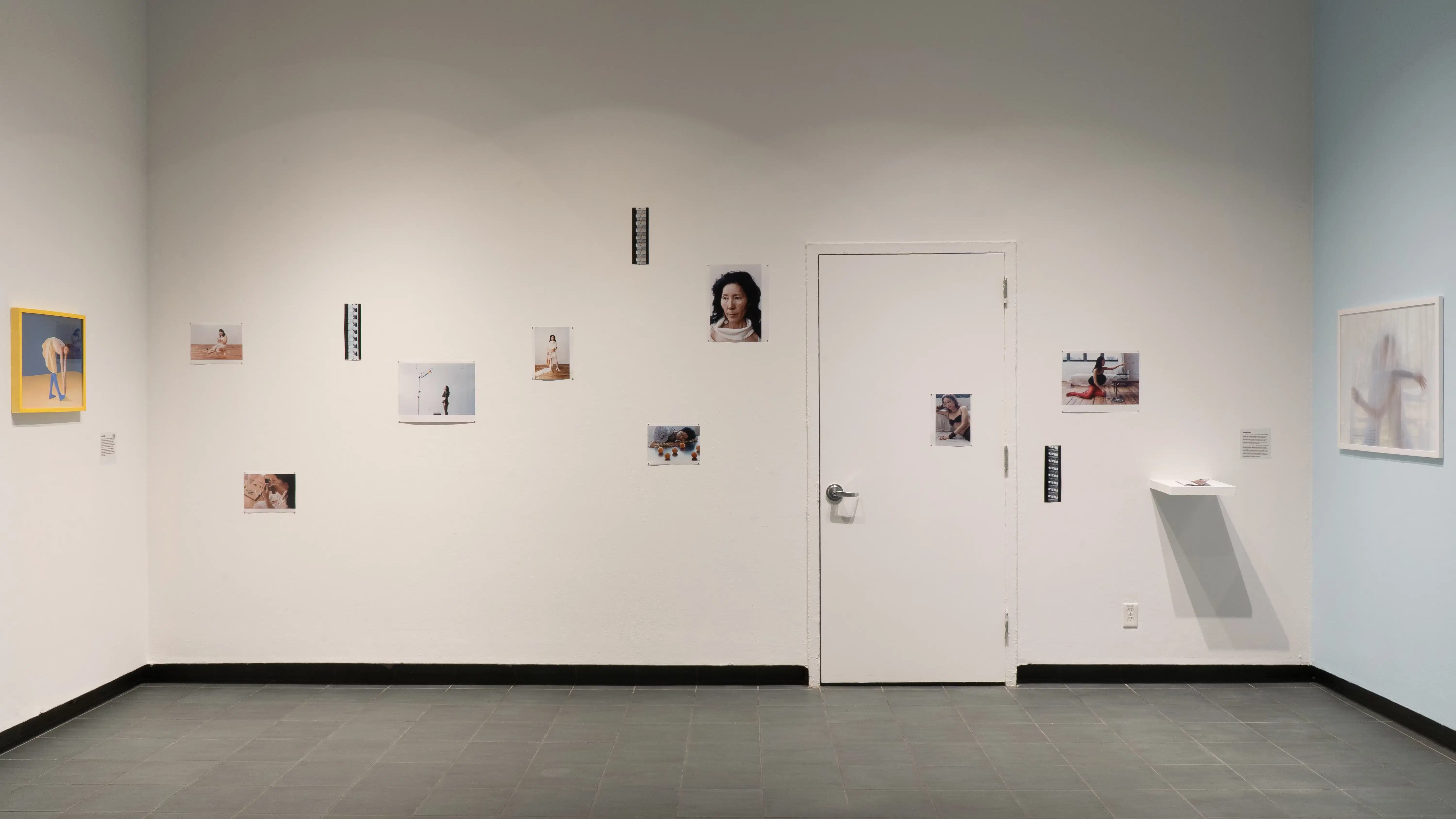 Photographs on a wall in the gallery lobby. The images are spread widely, and there’s a lot of space between them.