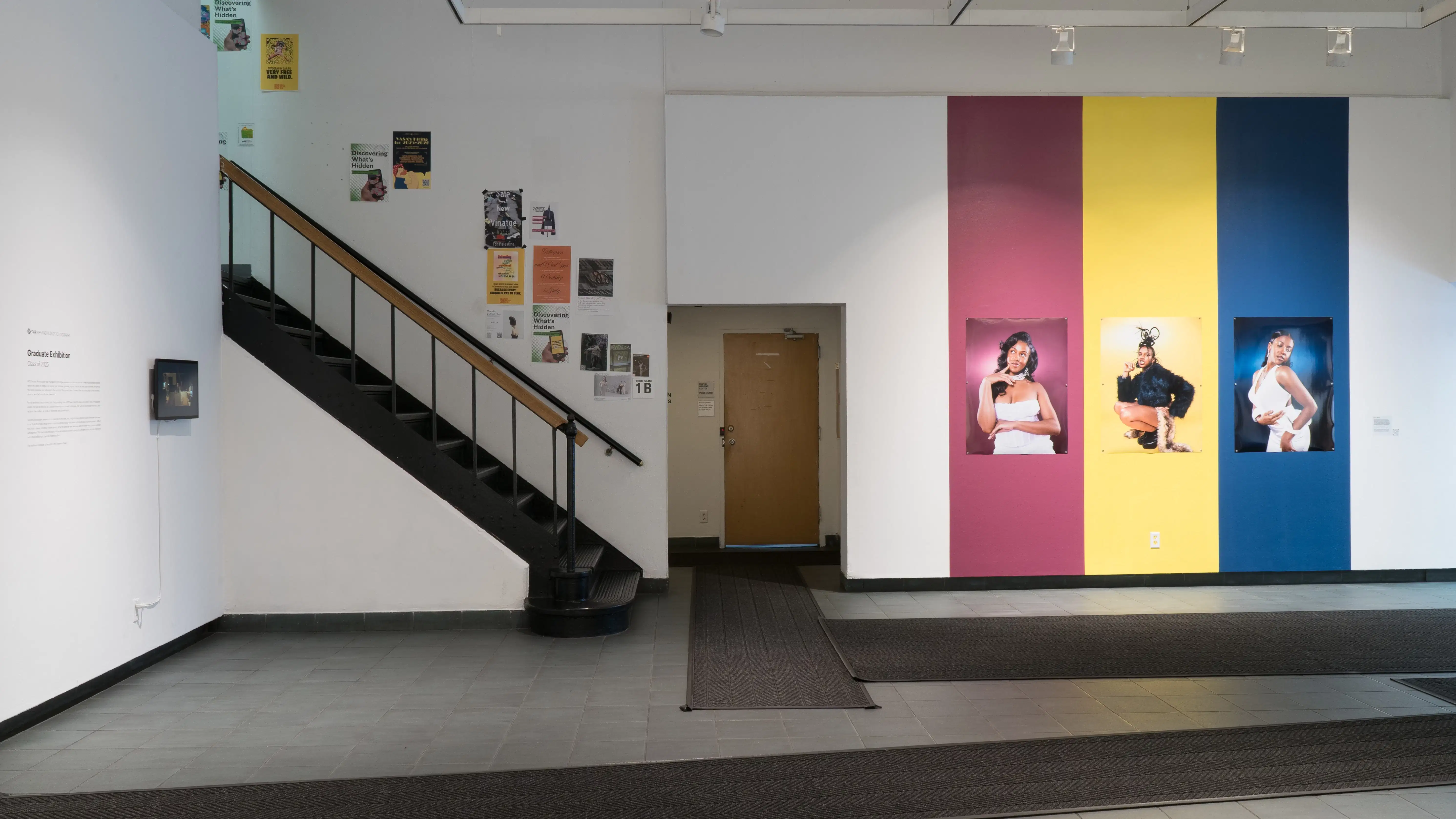 The lobby of the SVA Gramercy Gallery featuring work by a student. Three large vertical stripes of pink, yellow, and blue are painted on the wall. Photographs of a model posing are hung on these stripes.