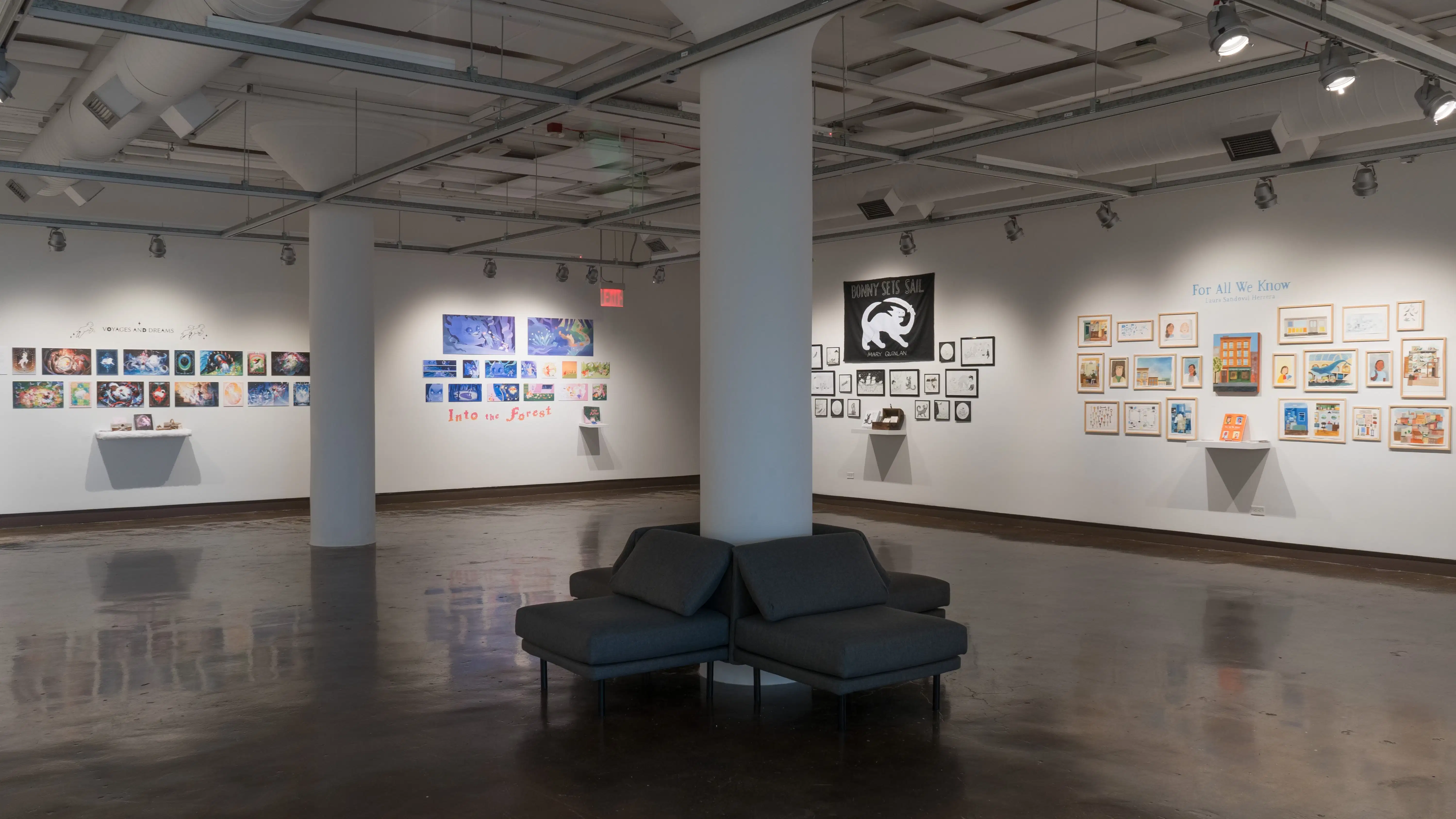 An overview shot of Gallery 1 at the SVA Chelsea Gallery. There are chairs surrounding a column in the foreground, and lots of colorful prints on the walls in the background.
