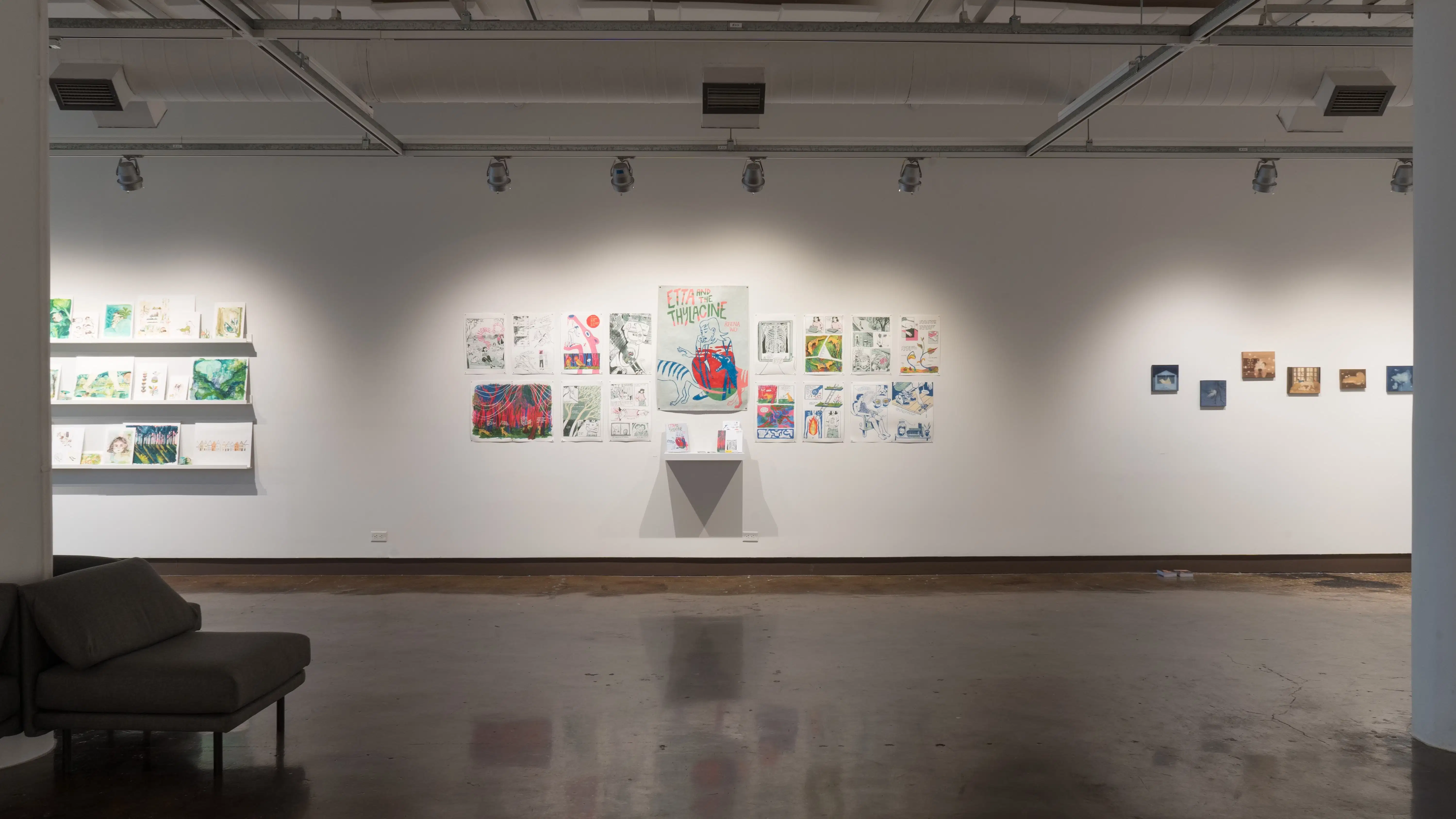 A straight view of the west wall at the SVA Chelsea Gallery. There are three projects visible on the wall: watercolor paintings on shelves on the left, two rows of pinned illustrations in the middle, and small paintings on panel on the right.