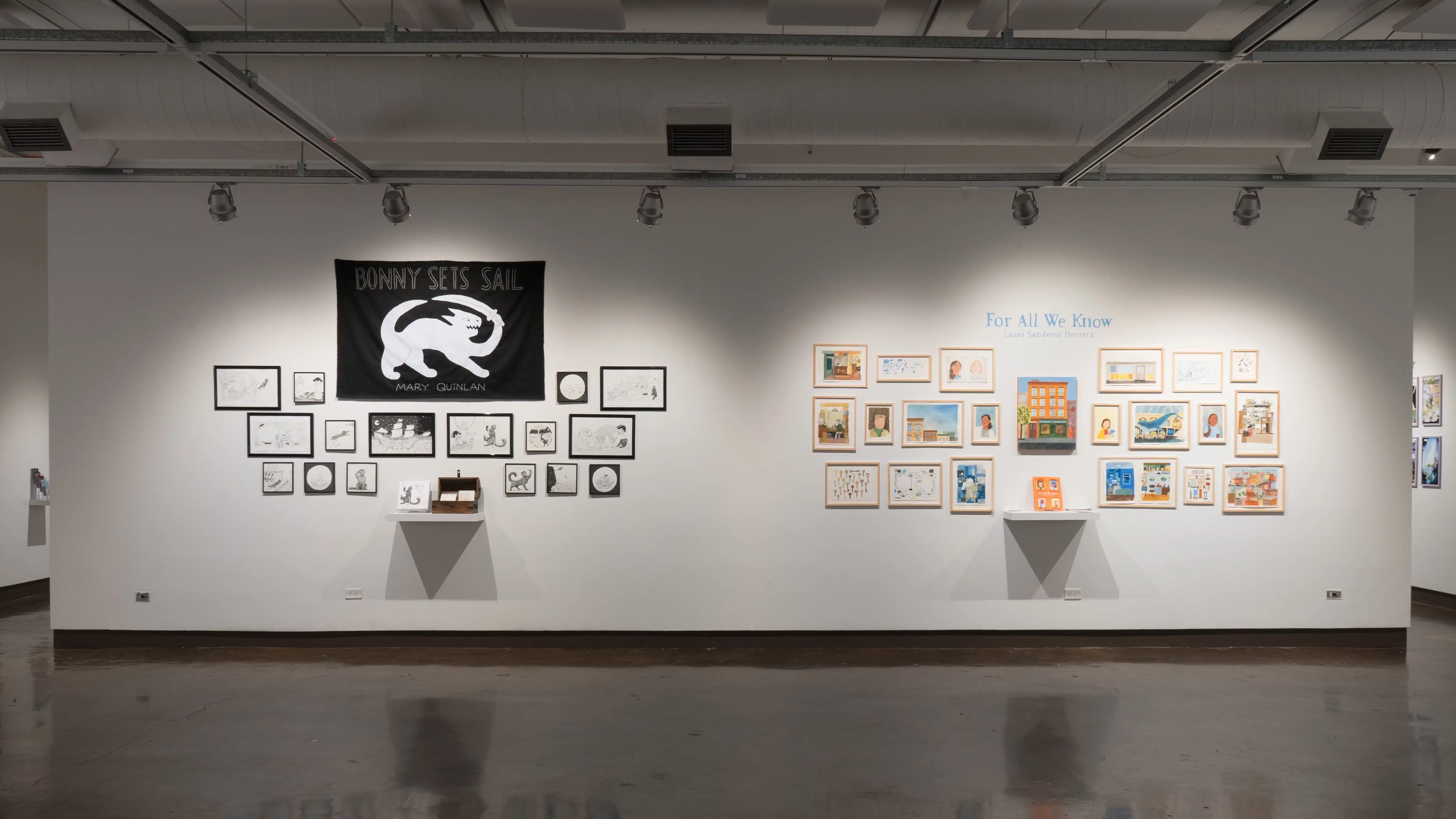 A view of the east wall at the SVA Chelsea Gallery. On the left is a black and white project hung salon style. There is a large black flag with a cat with a sword in white at the top, under the words, “Bonny sets sail.” Another project hung salon-style is on the right, with many colorful framed prints under the title, “For All We Know.”