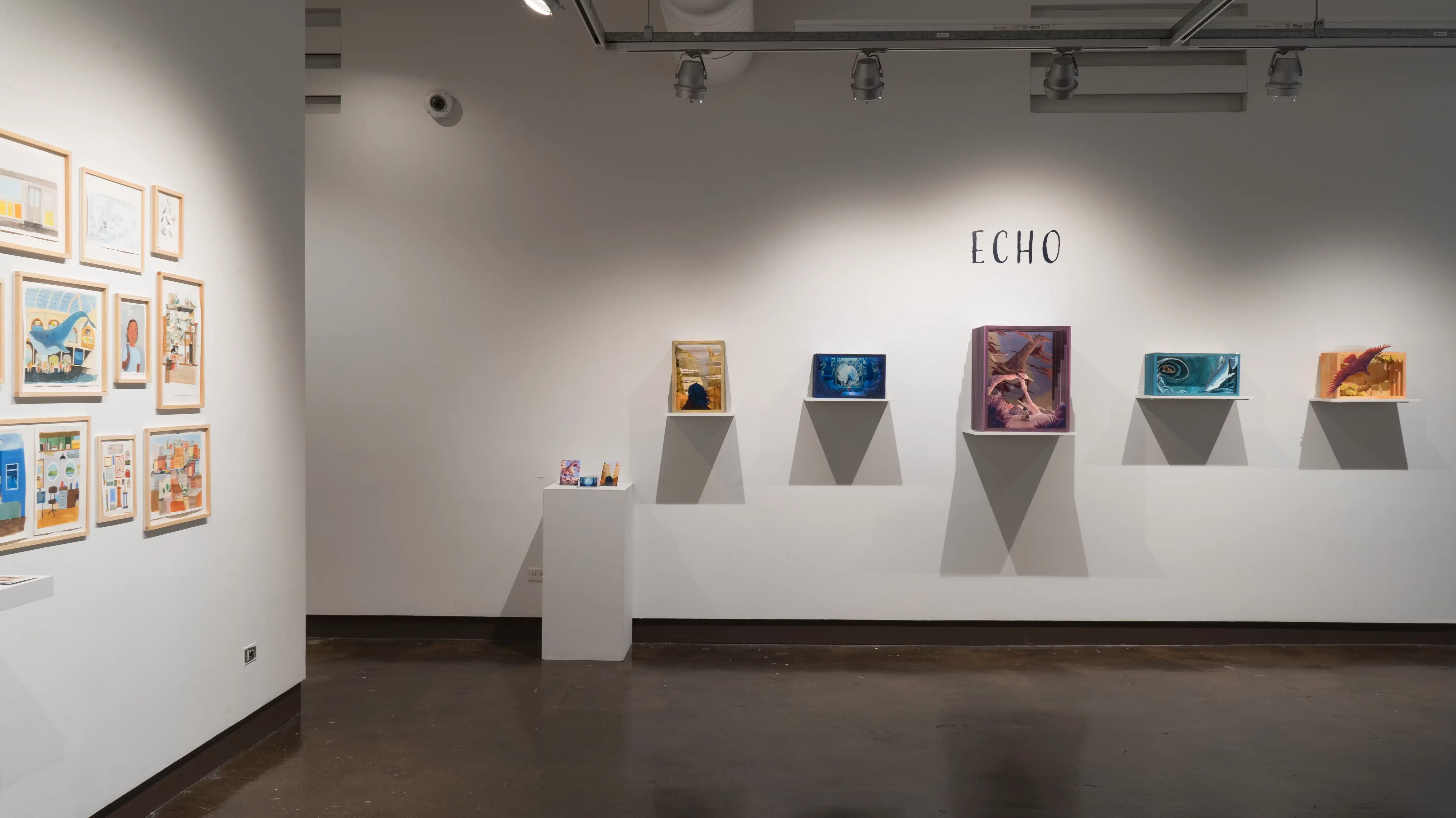 A view of the east and south walls of Gallery 1 at the SVA Chelsea Gallery. There is a project of three dimensional wooden boxes showing different outdoor scenes. There is a pedestal with postcards to the left.