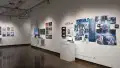 On a wall of gallery two, there are prints hung next to a monitor and headphones. Further to the right, another project’s prints are organized into a constellation, and a red string leads between images like a detective’s investigation board. A small radio and lamp sit on the pedestal beneath them.