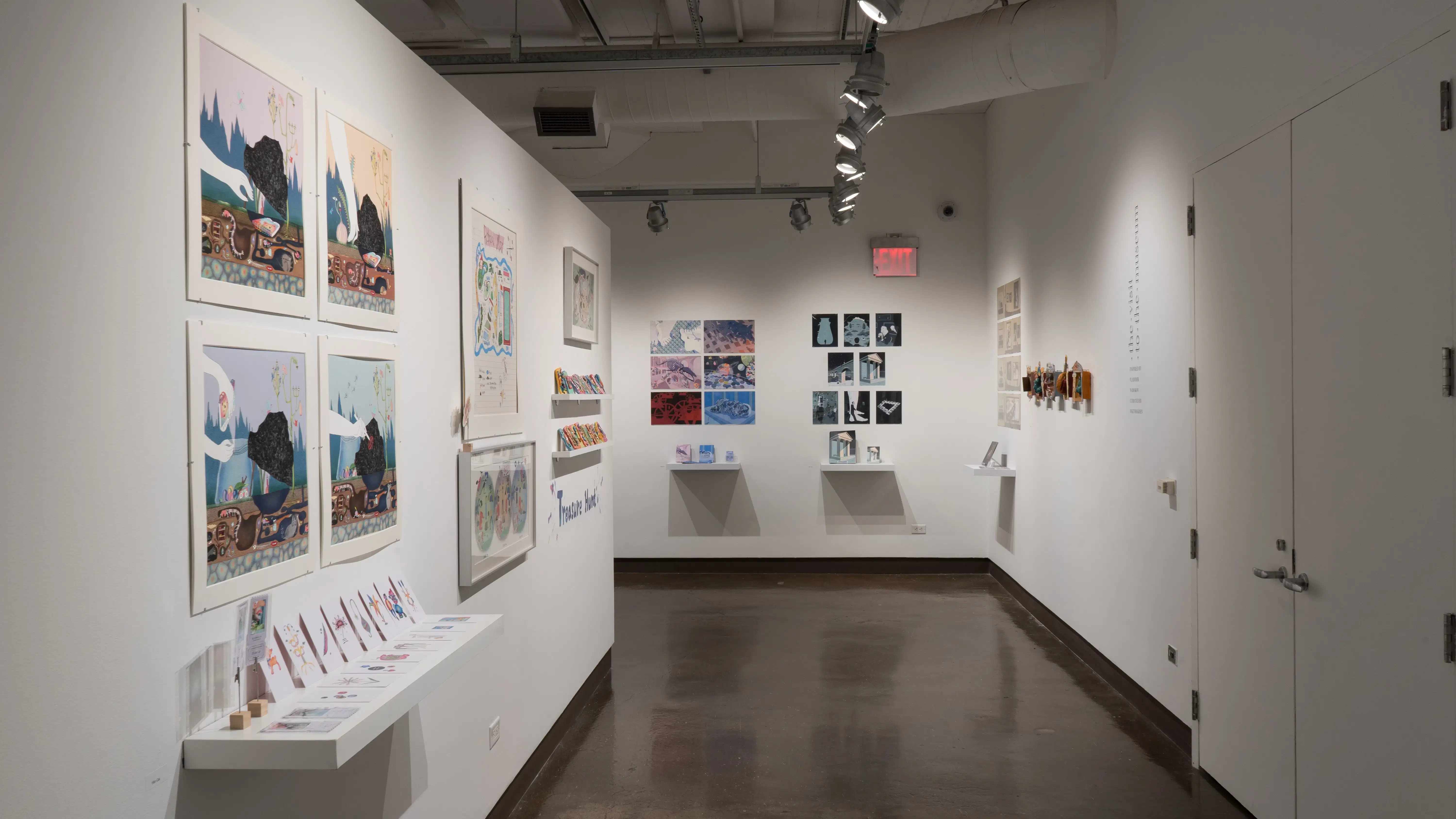 In the right hallway leading from gallery three to gallery four, framed and matted illustrations line the left wall. Straight ahead, prints arranged in grids hang on the wall above books on shelves.
